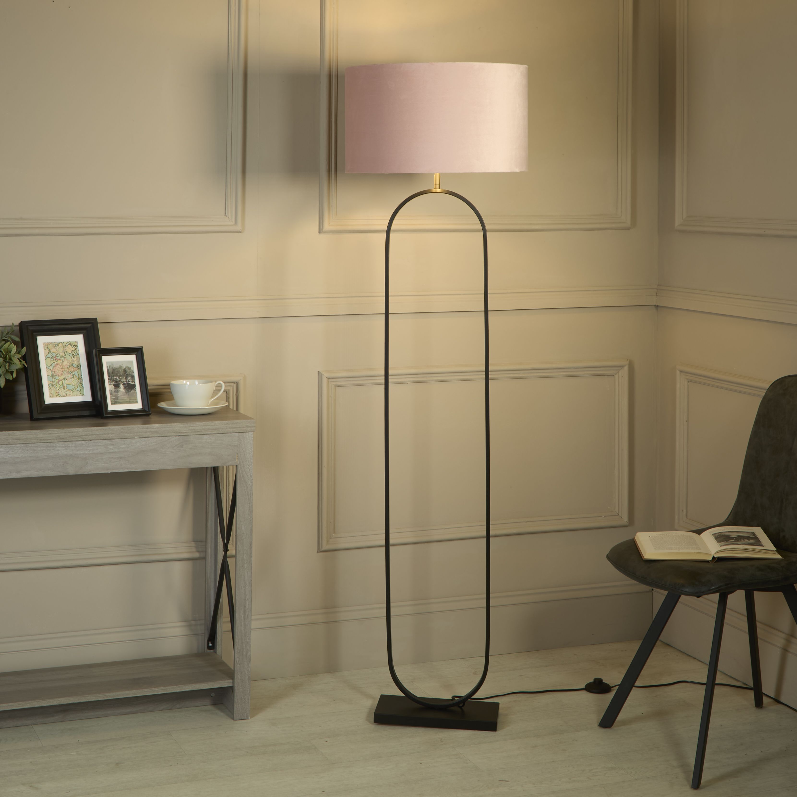 Modish floor lamp with pink velvet shade styled in a living room corner beside a console table and a black chair with an open book