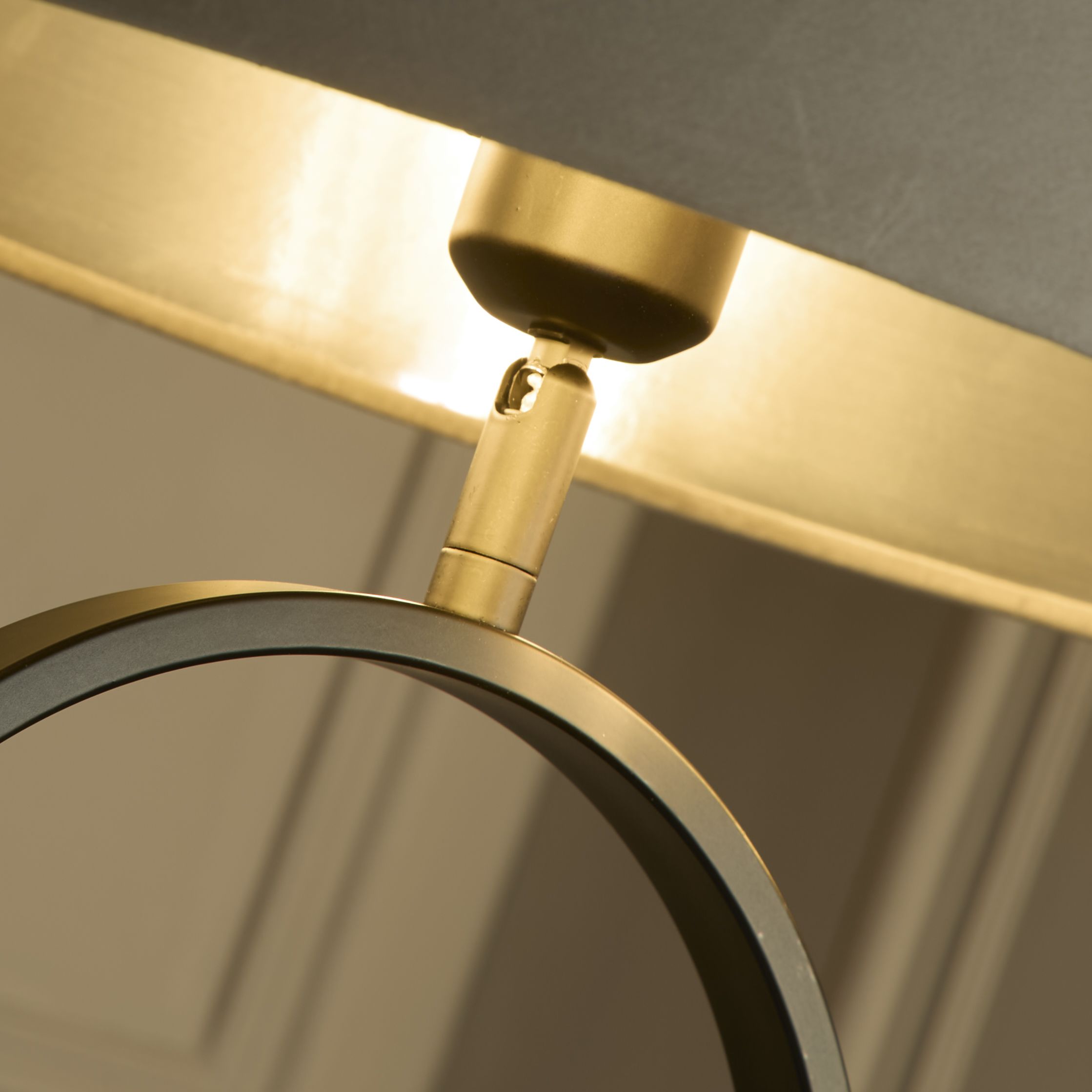 Close up of the brass adjustable joint connecting the taupe velvet shade to the black oval ring base