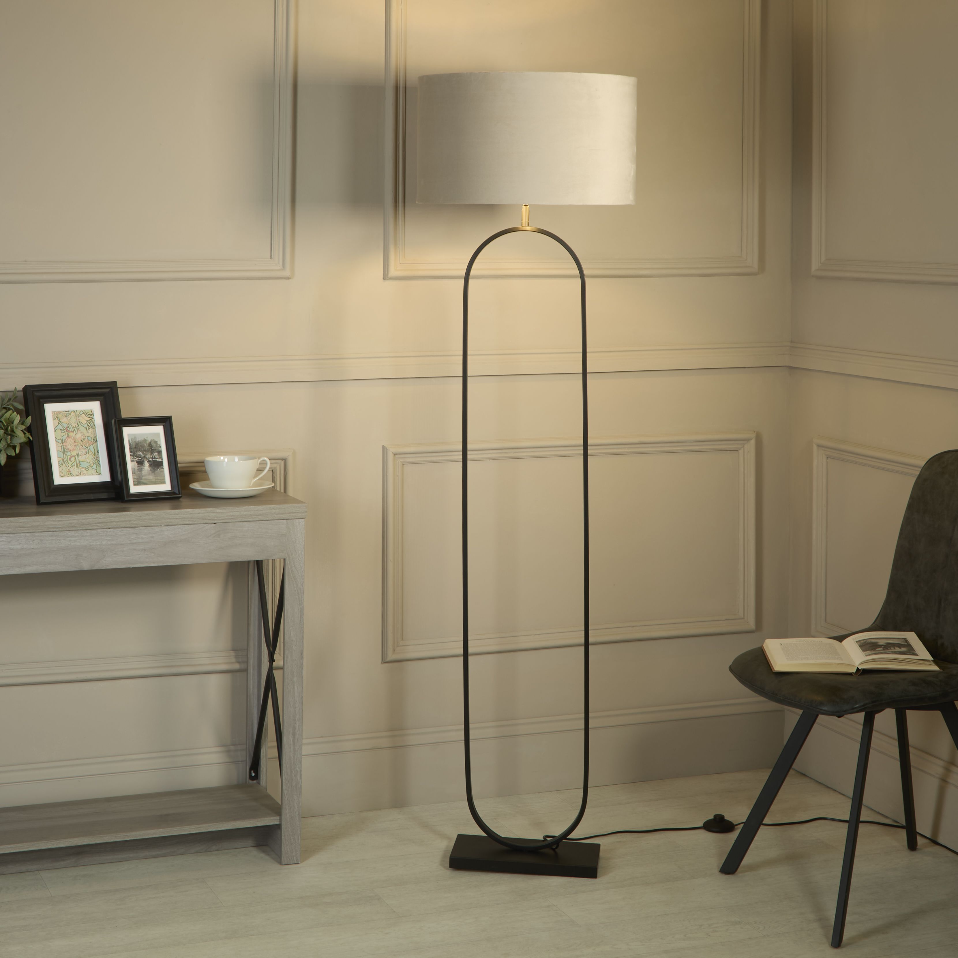 Modish floor lamp with taupe velvet shade styled in a living room corner beside a console table and a black chair with an open book