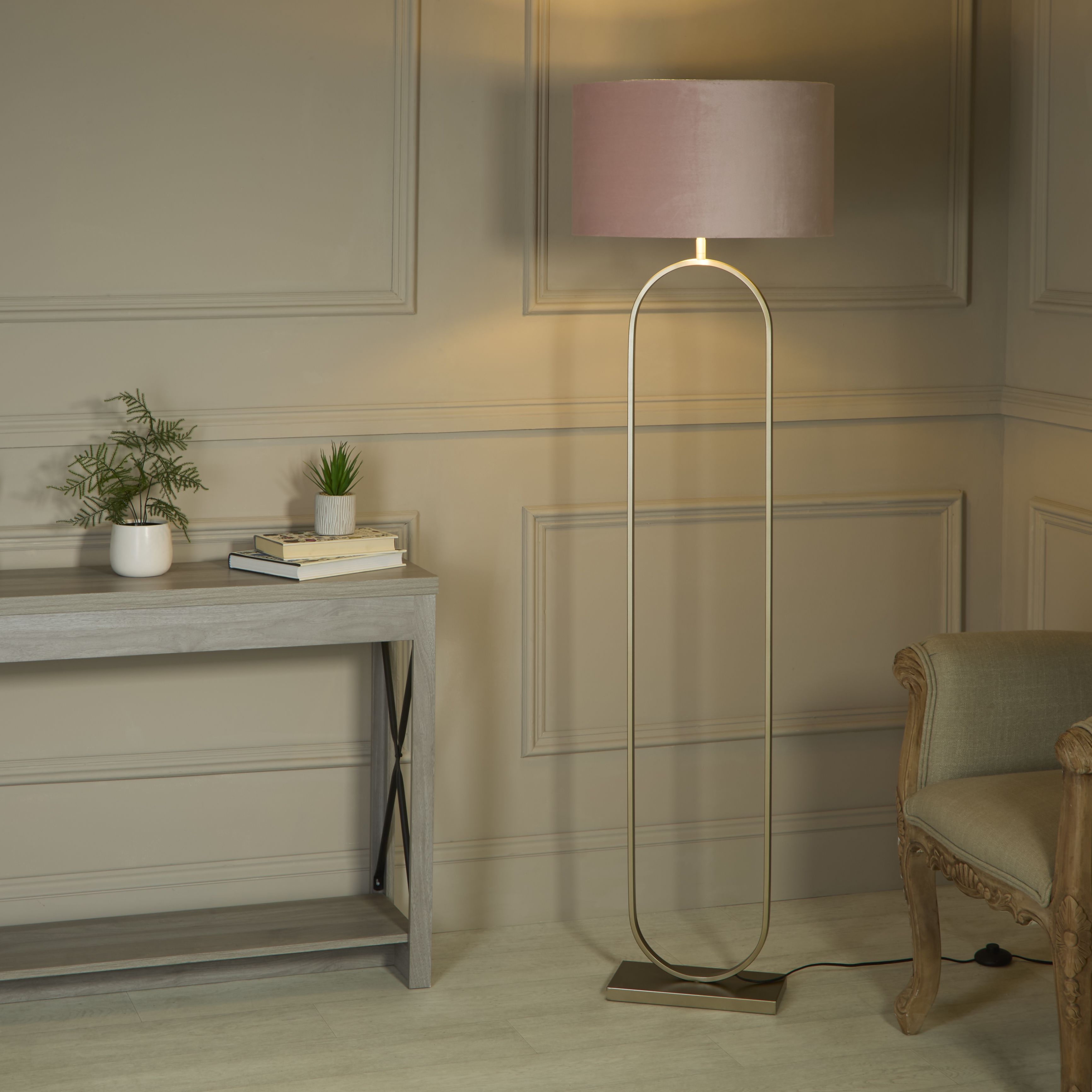 Modish floor lamp with pink velvet shade styled beside a console table with plants and books in a panelled living room