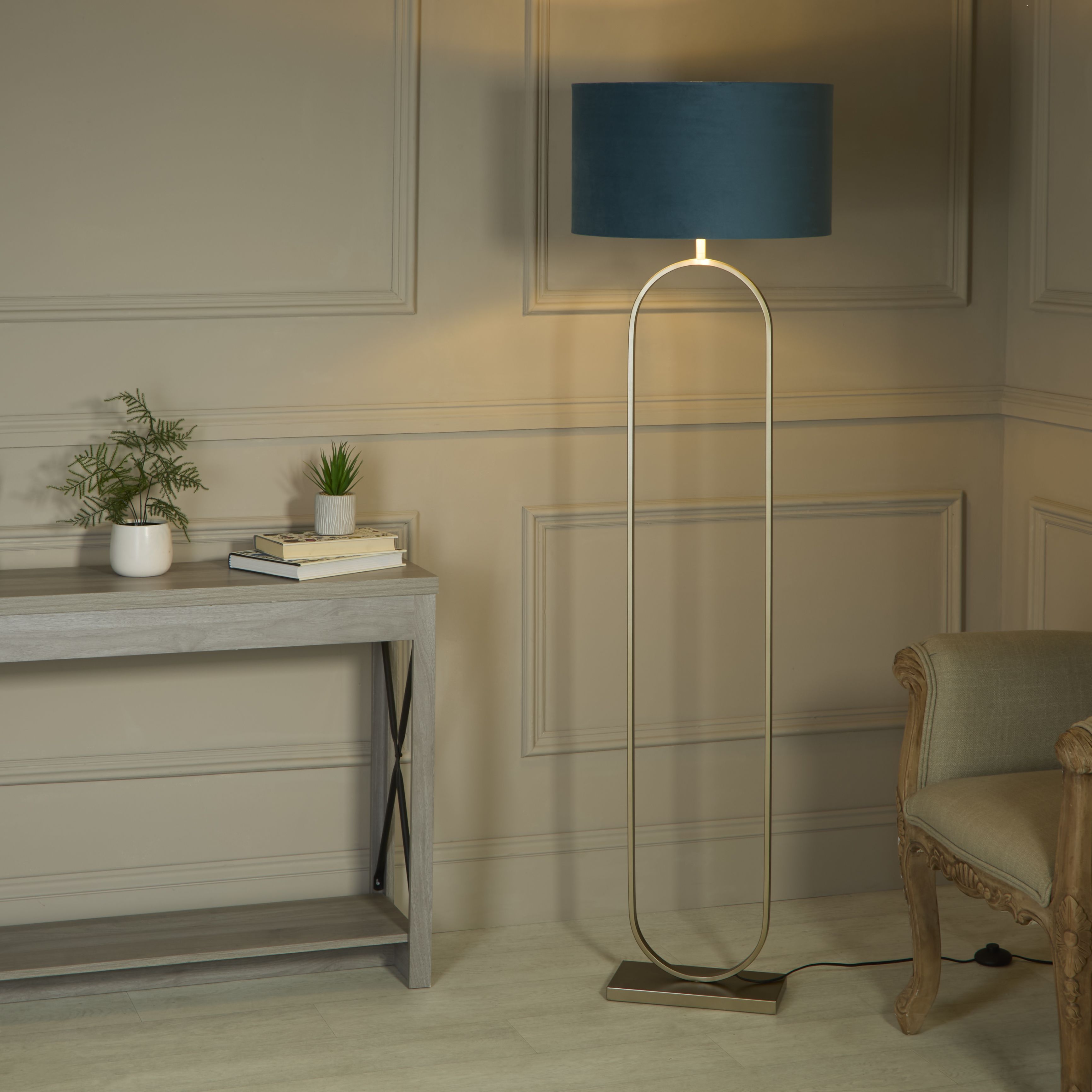 Modish floor lamp with teal velvet shade styled beside a console table with plants and books in a panelled living room