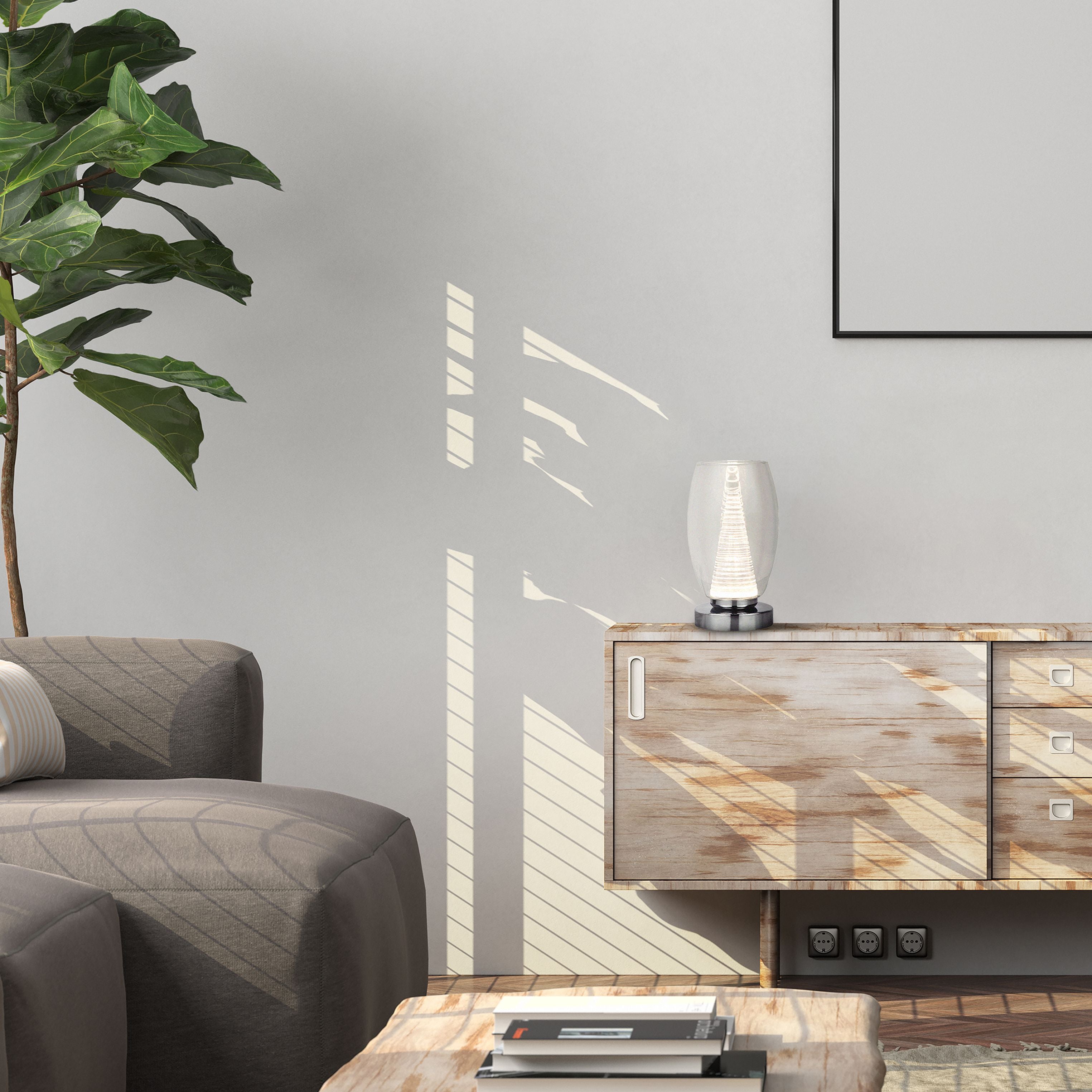 Searchlight Cyclone table lamp in chrome and clear glass styled on a wooden sideboard in a living room, next to a potted fiddle leaf fig