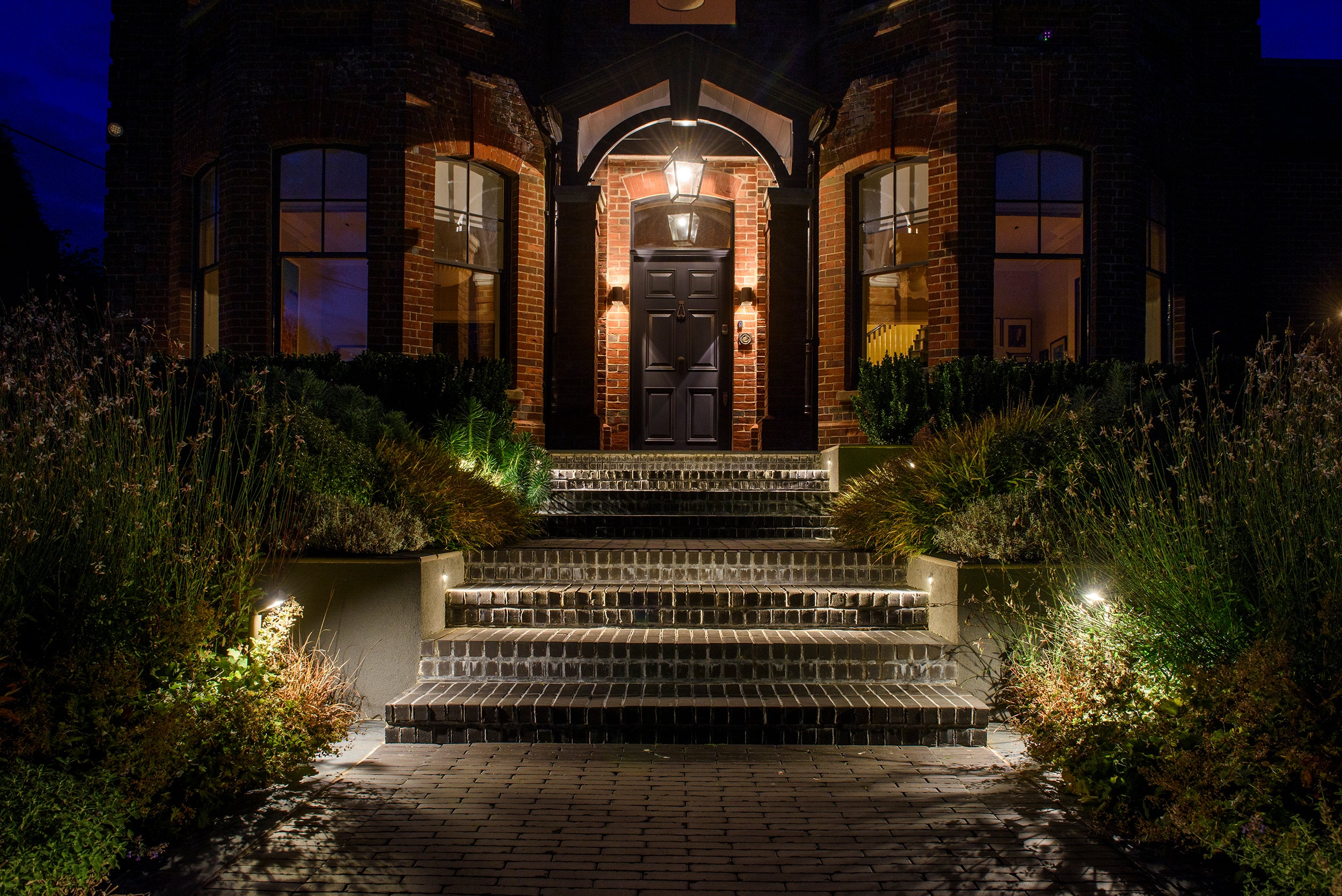 Stately home entrance with steps at night, illuminated by outdoor lights.