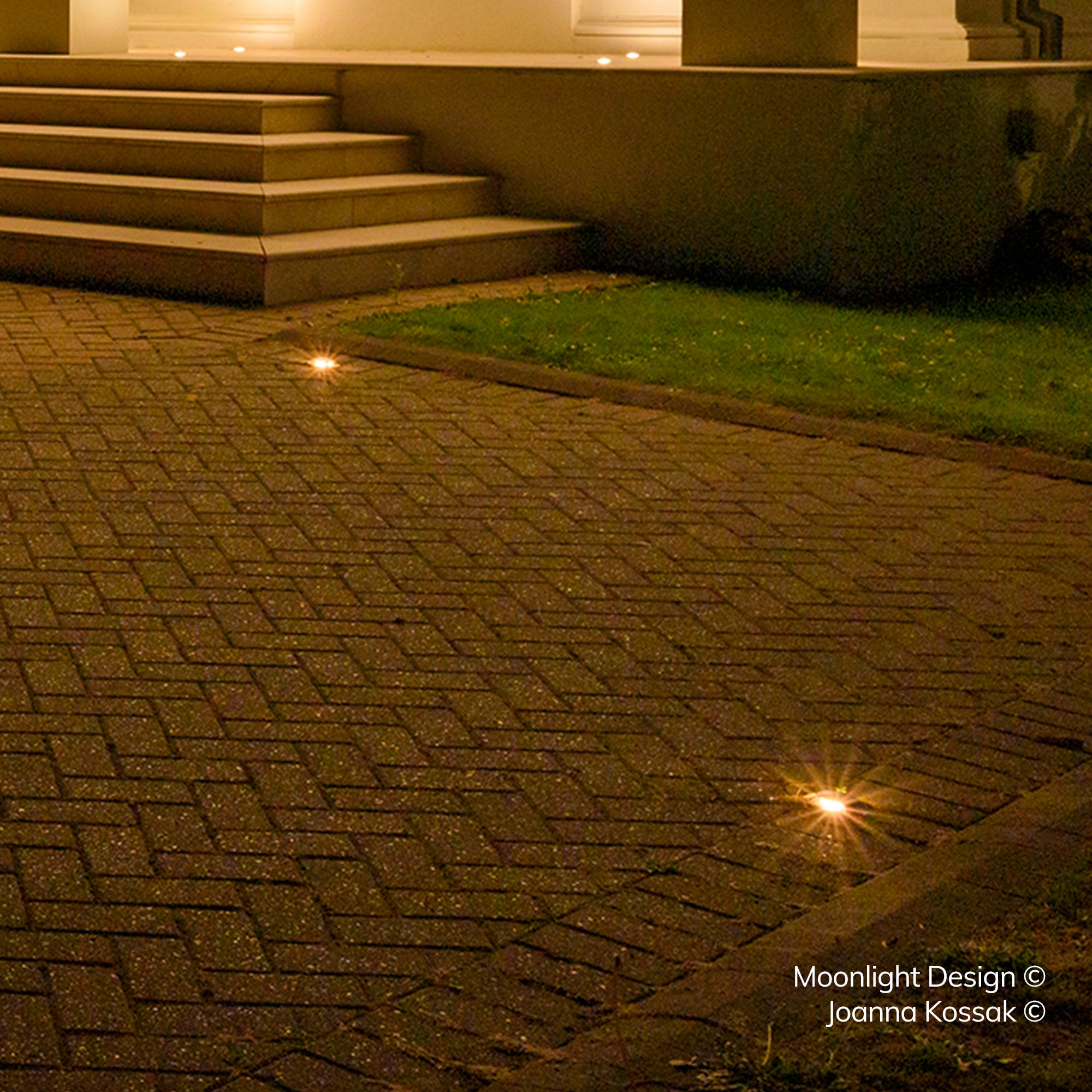 A herringbone brick driveway and lawn beside a stone staircase at night, with several recessed Hunza Path Lights dotted across the paving and steps above. A Moonlight Design installation, not stock imagery.