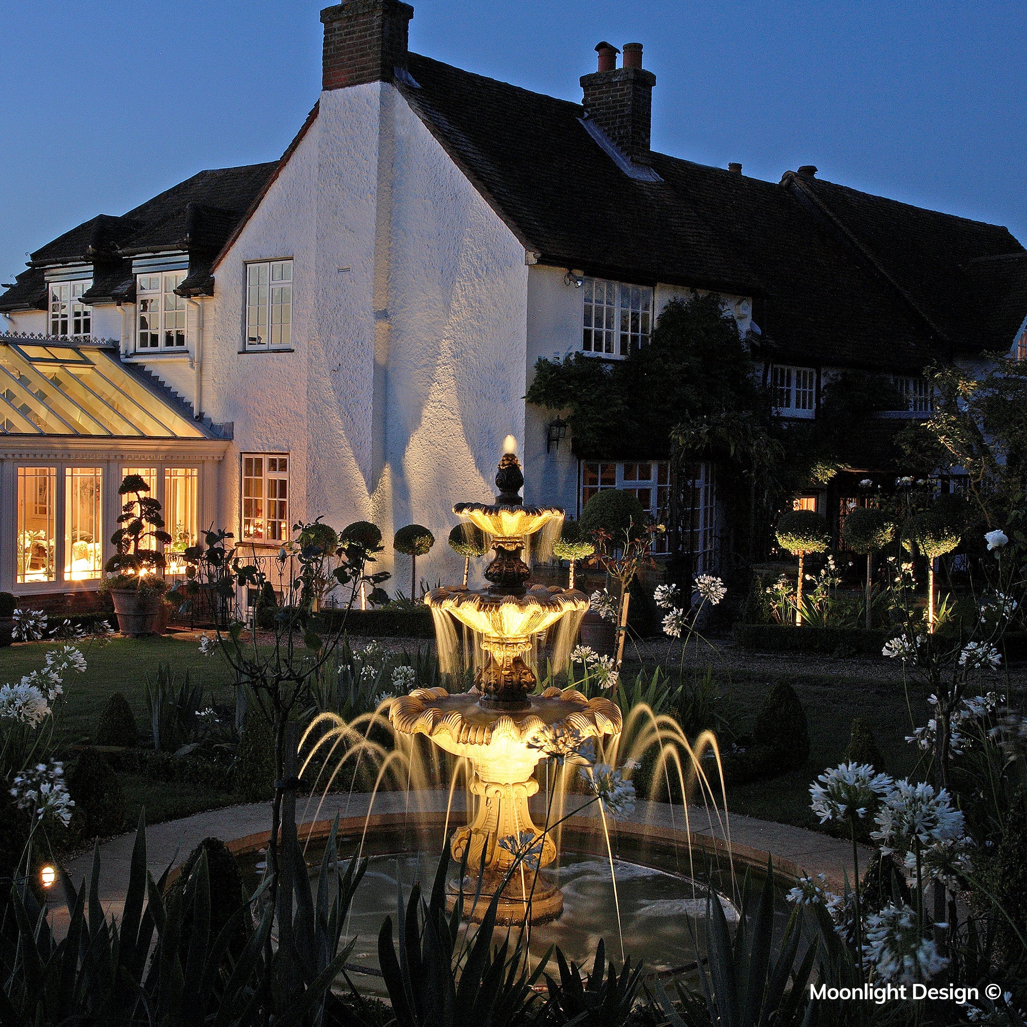 Discreet Hunza pond lights enhance the formal fountain, highlighting the cascading water and adding warmth to the surrounding night-time garden. A completed Moonlight Design pond lighting project.