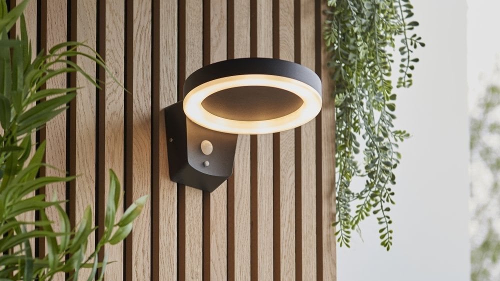 Wall-mounted light fixture on a wooden wall with plants.
