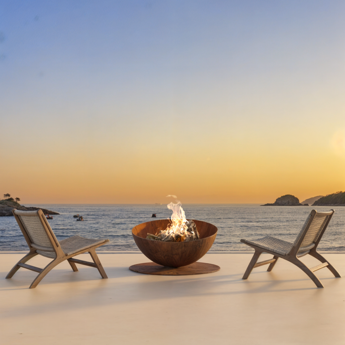 GlammFire Solace round Corten steel fire pit with flames on an open terrace overlooking the sea at sunset