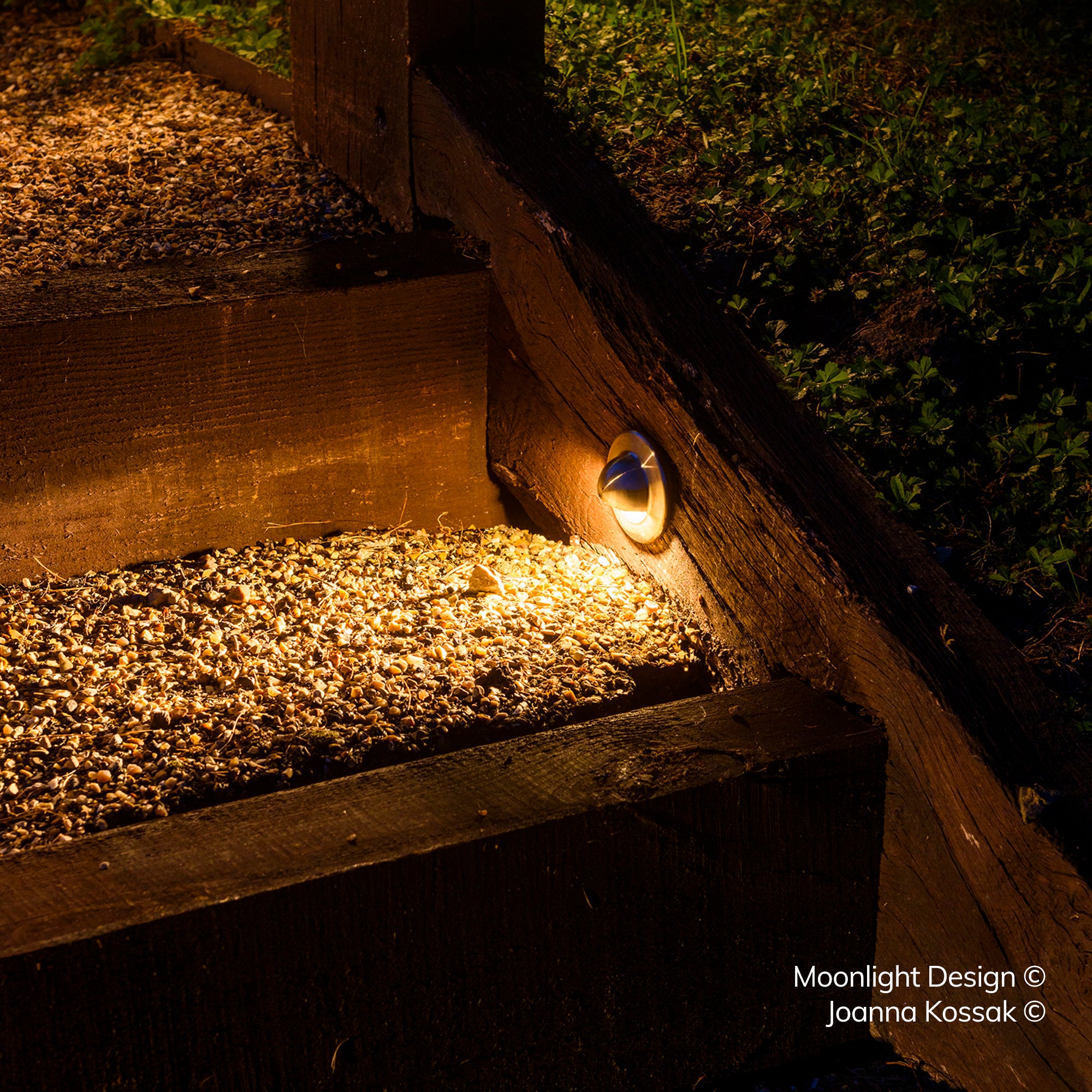 A Hunza eyelid step light recessed into a timber railway sleeper step, lighting the gravel tread below at night. A Moonlight Design installation, not stock imagery.