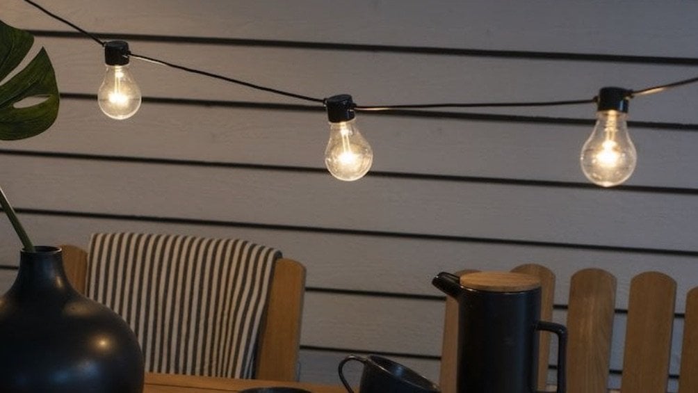String of illuminated light bulbs above a wooden table with decorative items.