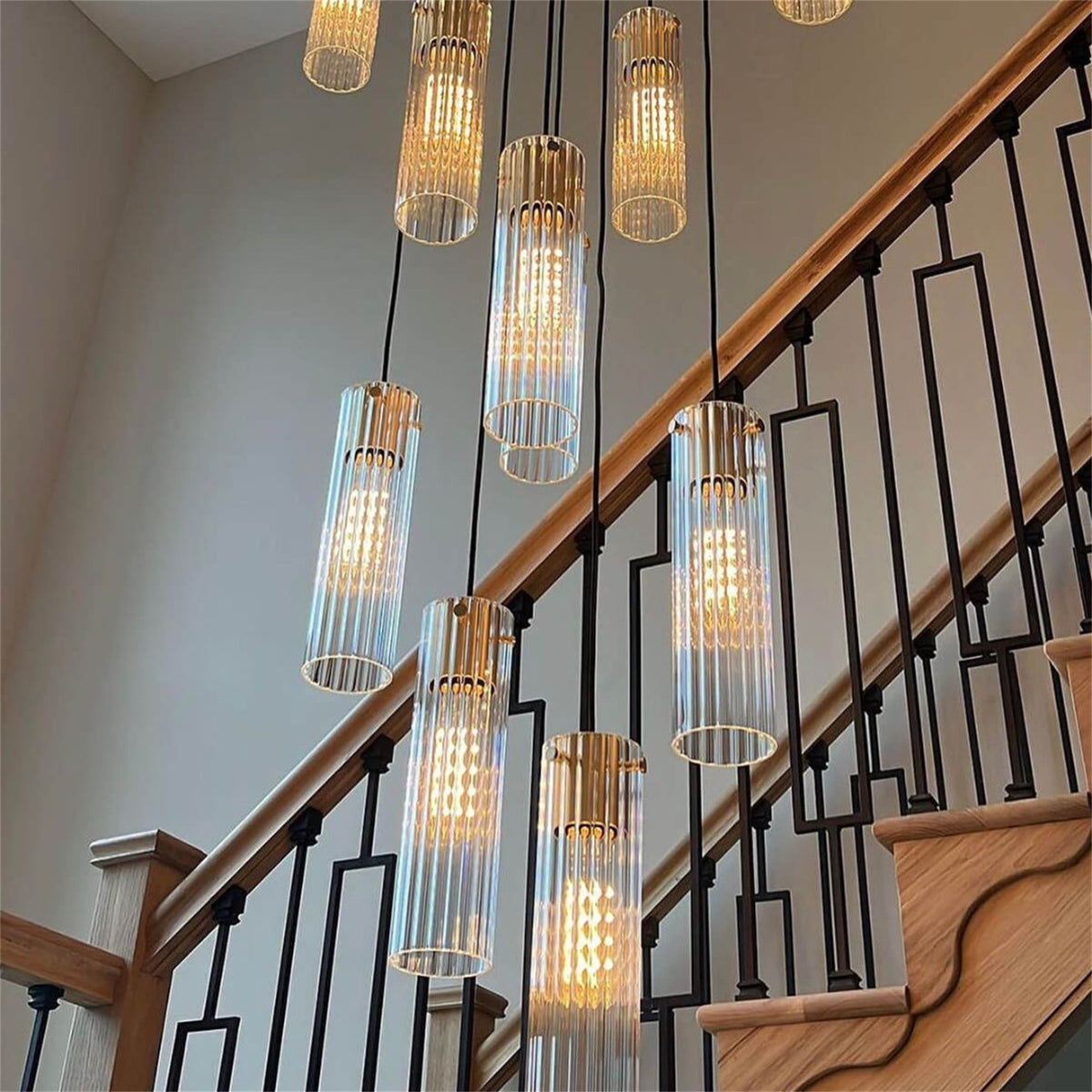 Lit clear ribbed and smooth teardrop glass pendants with brass coloured lamp holders hanging at different heights beside a tall window, from a Leverint cascade installation