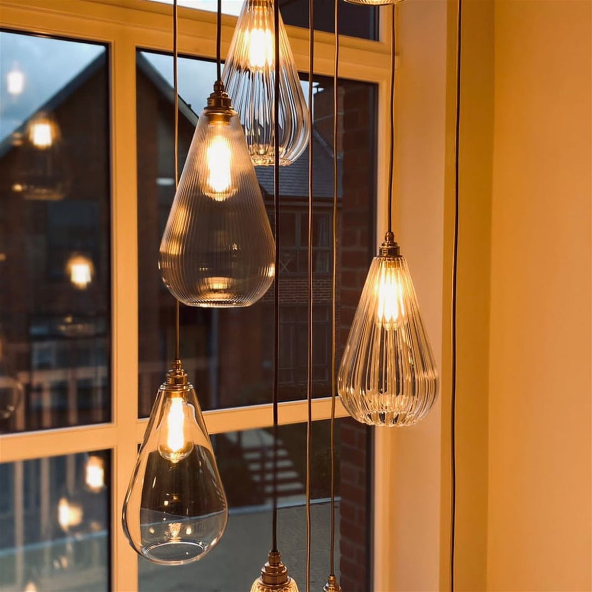 Teardrop shaped pendants in clear and ribbed glass hanging at different heights on dark flex in front of a tall window