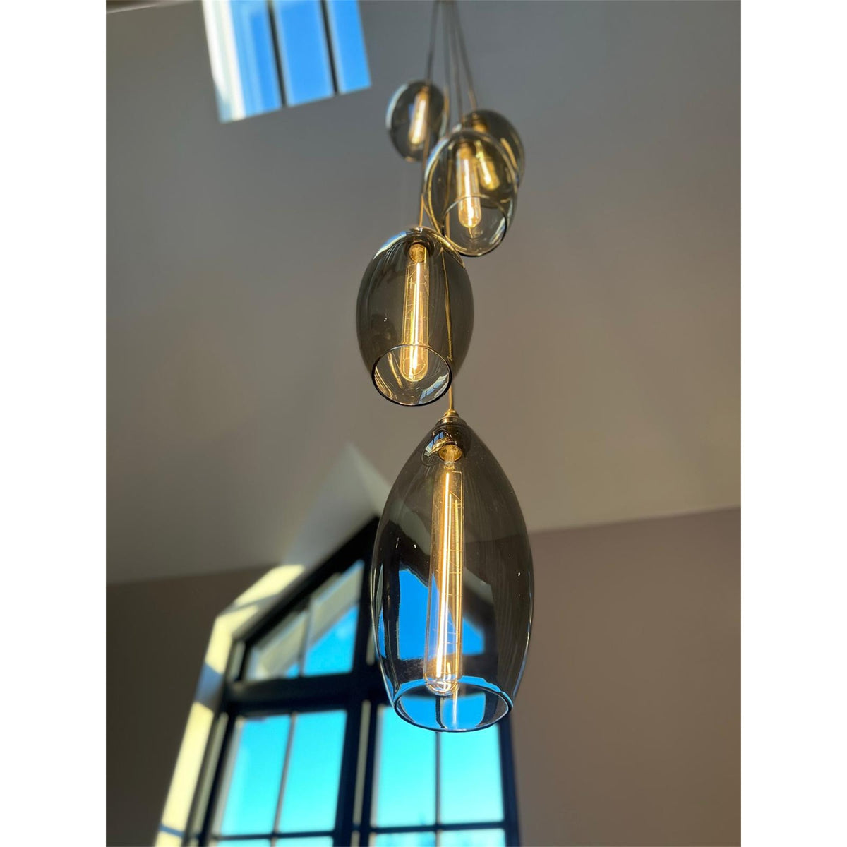 Leverint Bespoke Vertical Pendant Cluster, smoky grey glass pendants of different sizes hanging one below another with filament bulbs, photographed looking up towards a skylight