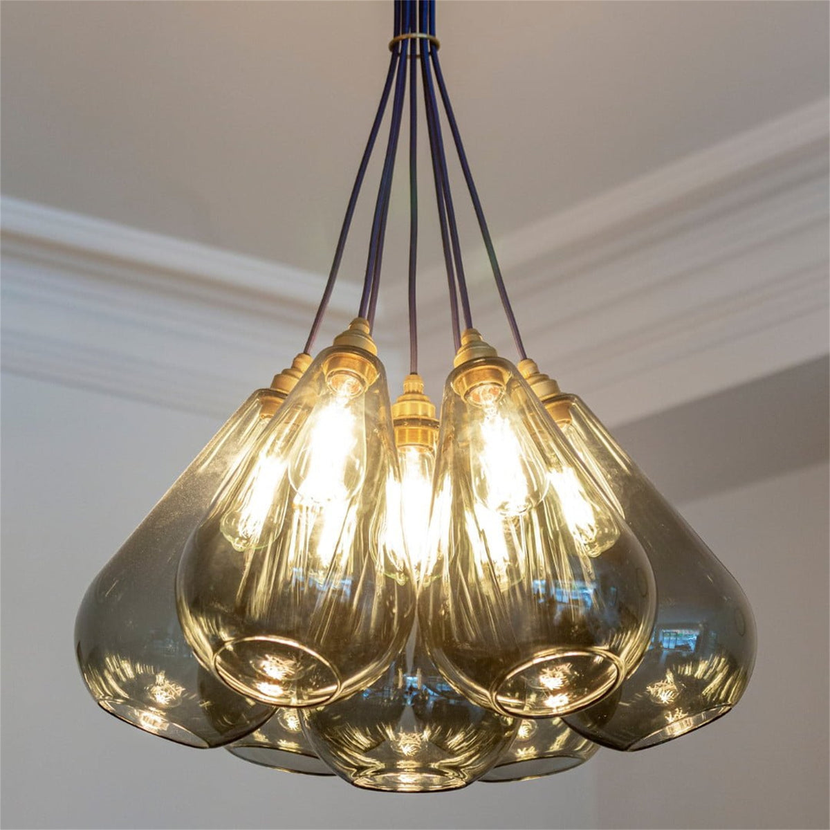 Cluster of lit Leverint Kingston teardrop pendants in smoky glass with brass toned fittings hung close together from dark cables