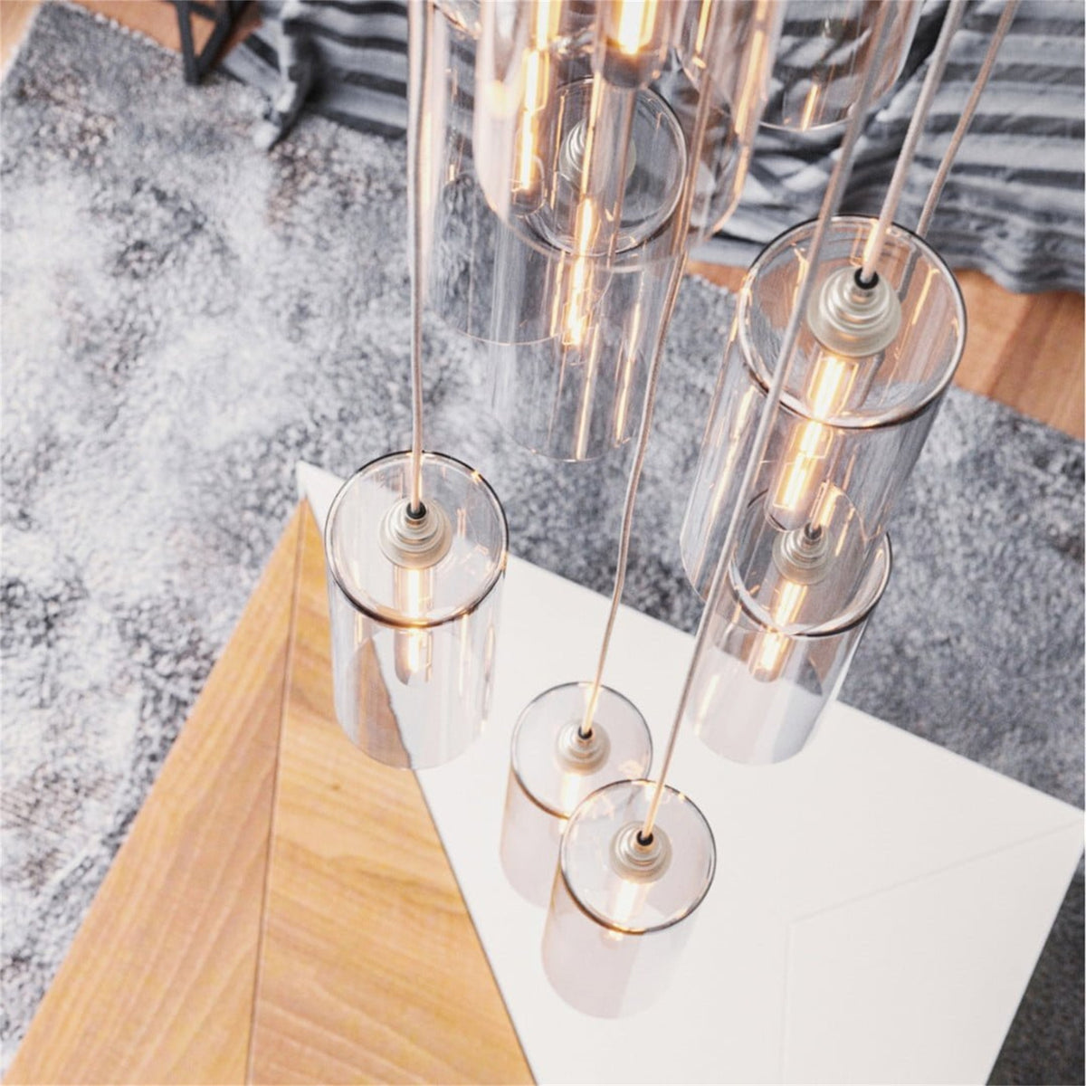Leverint Piccadilly cascade cluster of tall clear glass cylinder pendants hanging at different heights above a white table and grey rug, bulbs lit