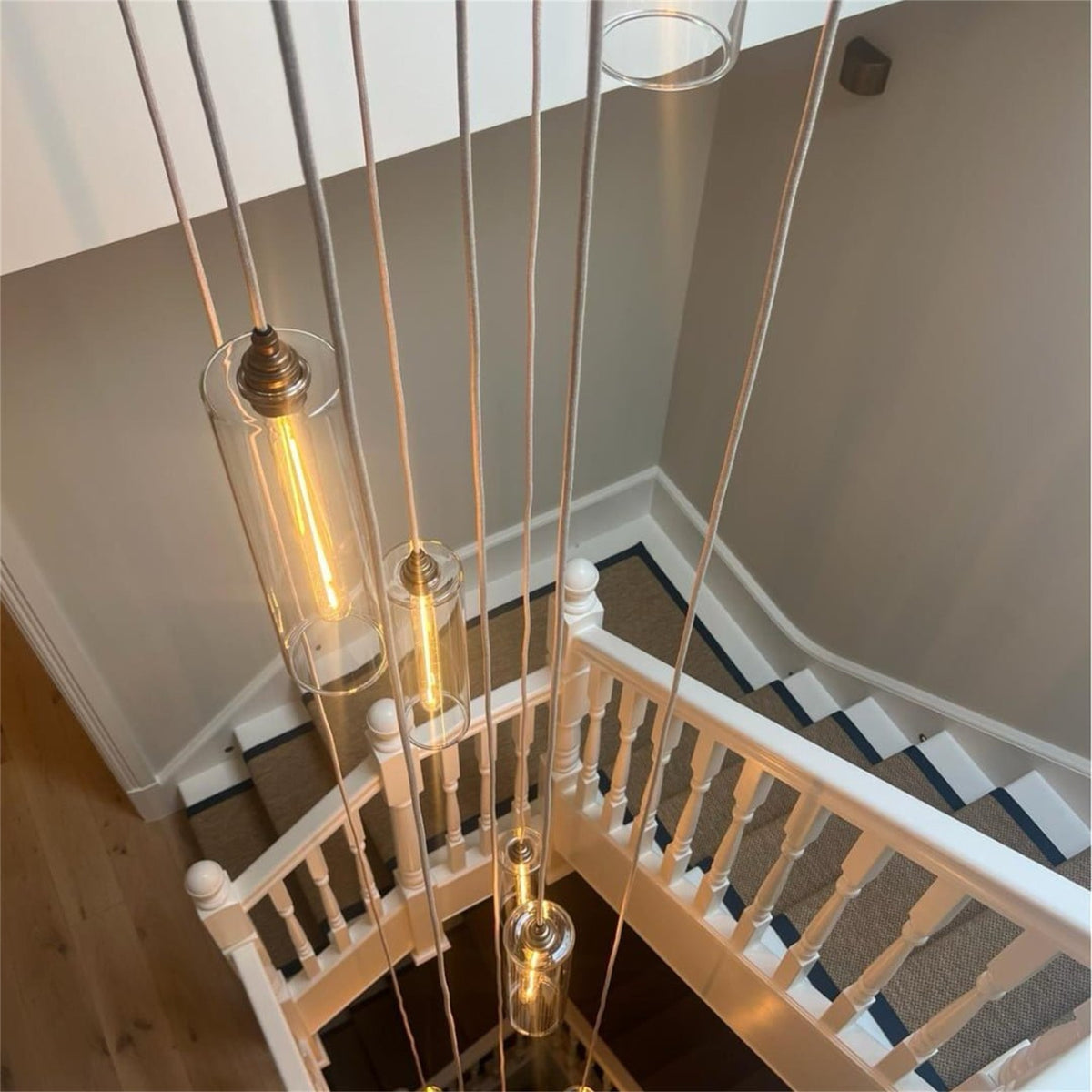 Leverint Piccadilly cascade cluster of tall clear glass pendants with lit filament bulbs hanging down a stairwell on long fabric cables