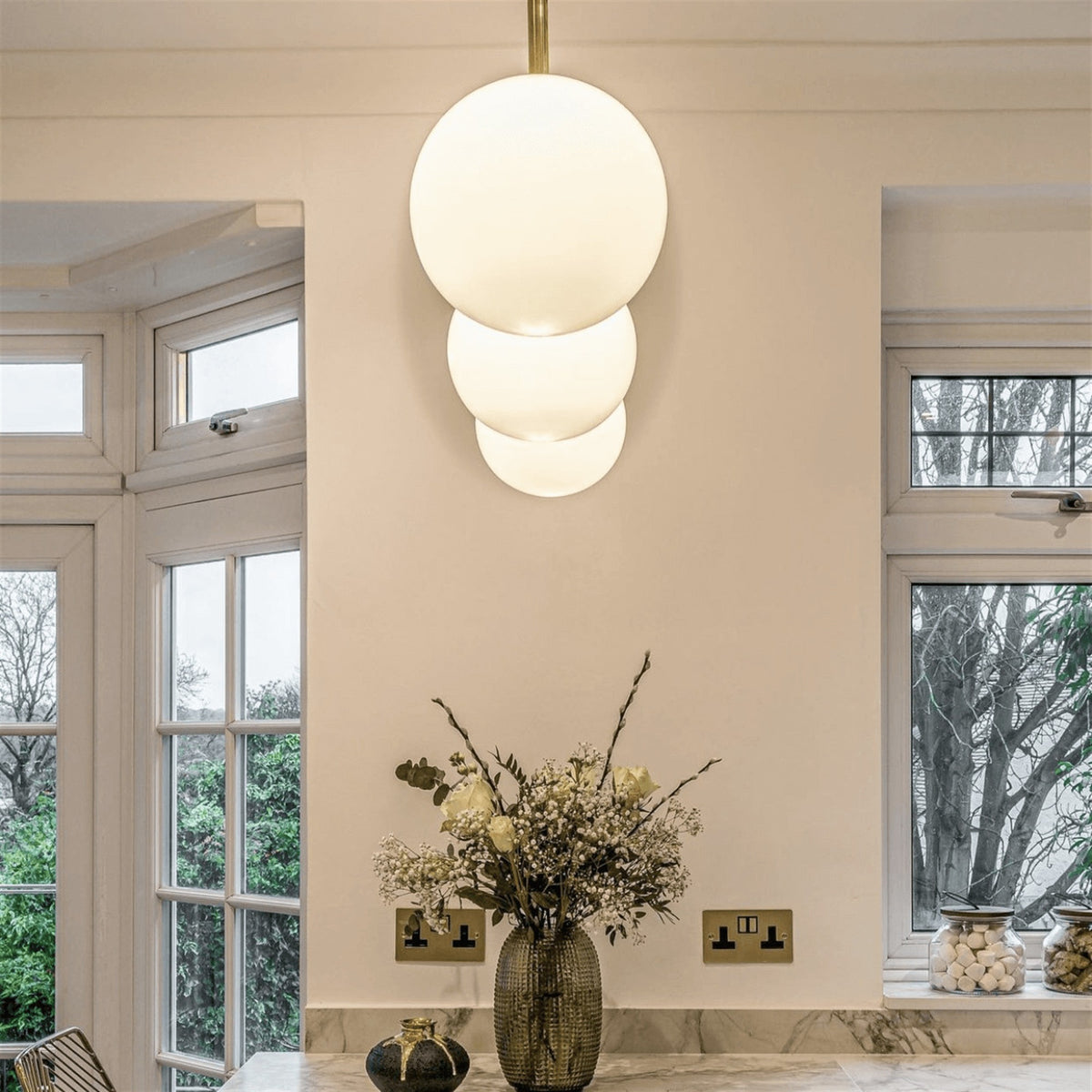 Leverint Pimlico sealed rod pendants as a vertical cluster of three opaque white glass spheres on a brass rod in a bright room with tall windows (lifestyle photo, size may differ from the Mini)