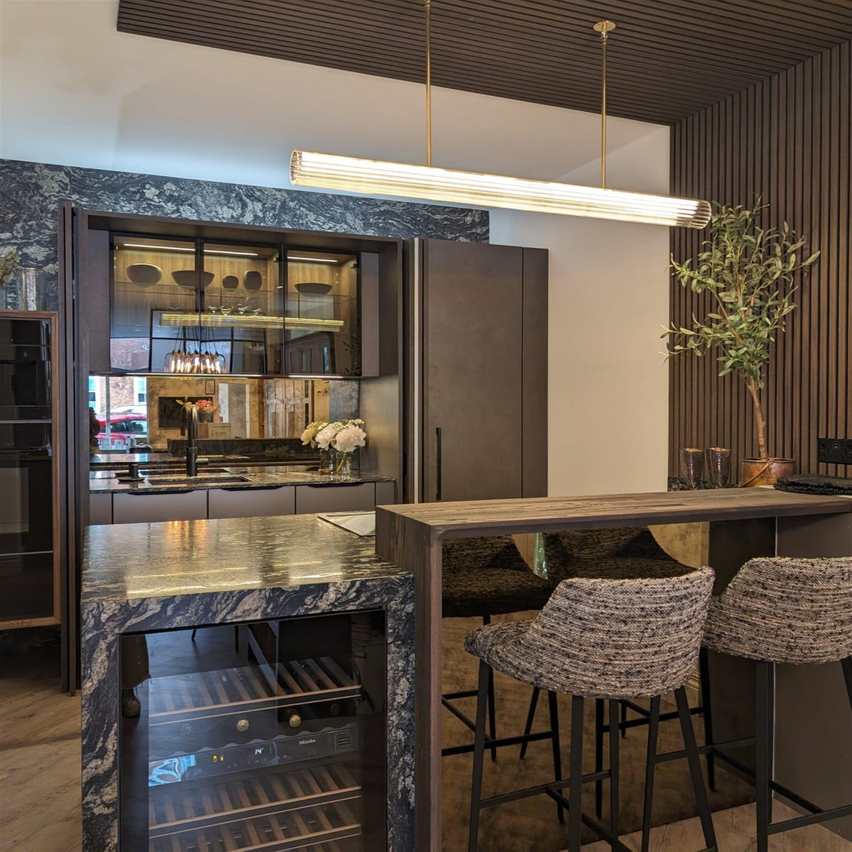 Leverint Temple Rod Pendant lit warm above a dark kitchen with slatted timber panelling and a stone worktop (lifestyle photo, length may differ from the Medium)