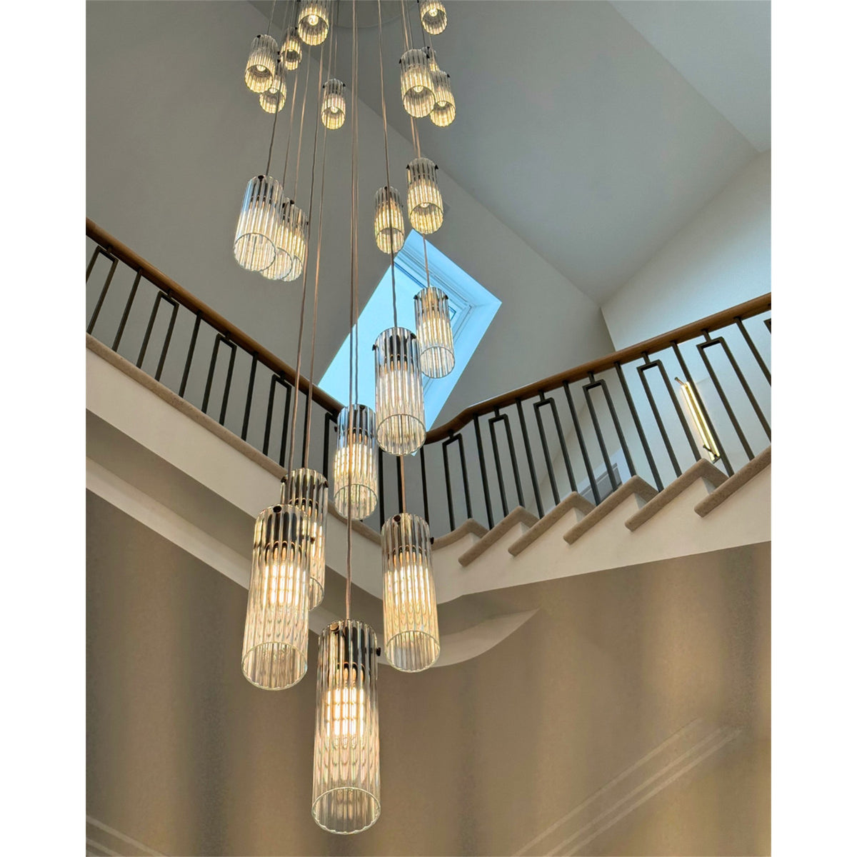 Leverint Temple pendant cluster of fluted glass cylinders hanging at different heights over a staircase with a dark balustrade and a skylight