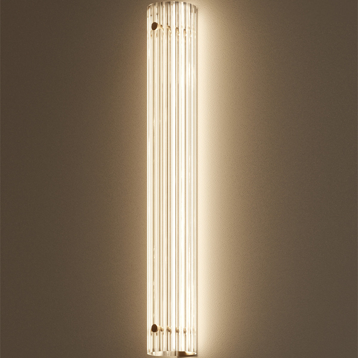 Single tall lit Leverint Temple Pillar Light on a warm taupe wall, ribbed glass column glowing with light washing up and down the wall