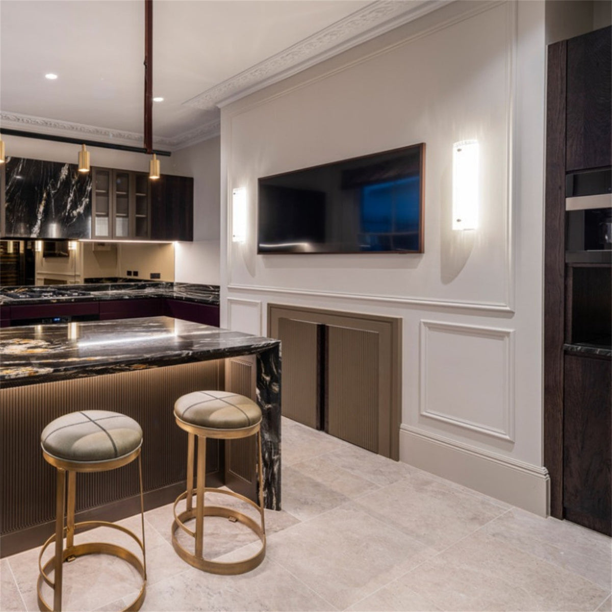 Pair of lit Leverint Temple Pillar Lights either side of a wall mounted television, with a marble topped kitchen island and bar stools beside them