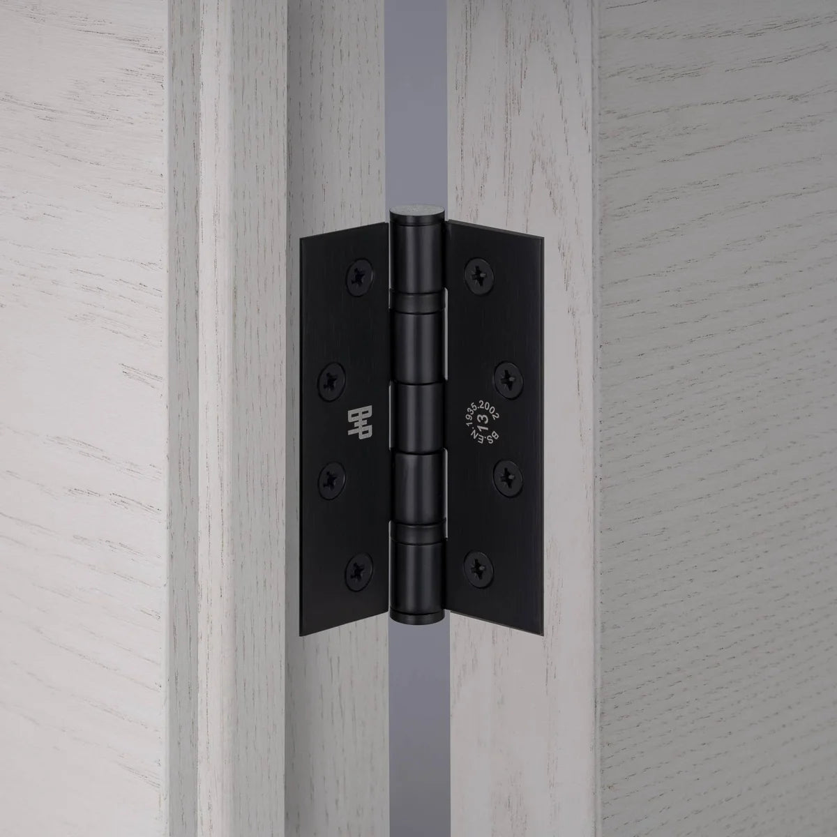 Buster + Punch black door hinge fitted between a pale grey oak door and frame, showing screws and engraved logo