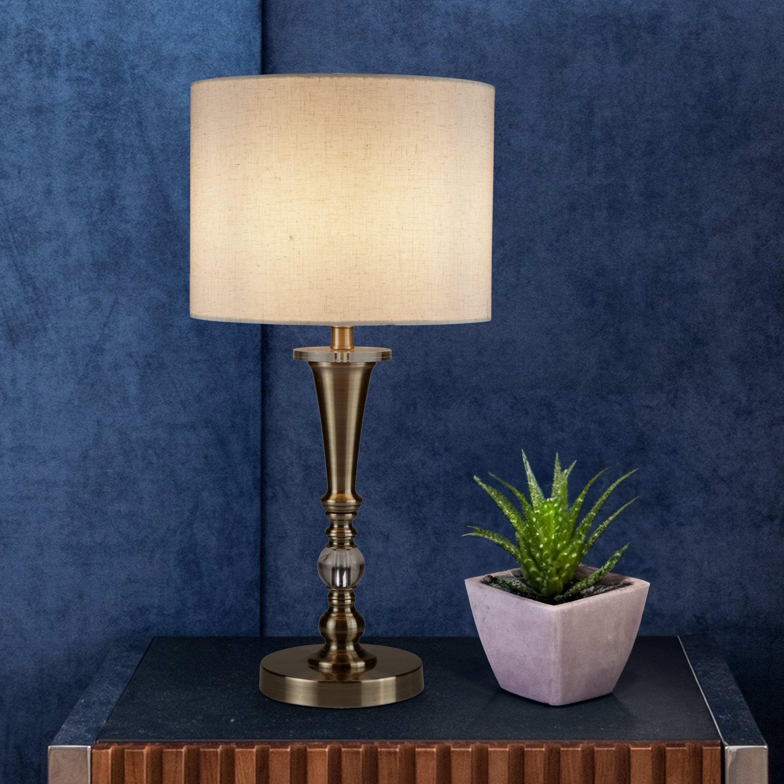 Oscar table lamp with oatmeal linen shade styled on a dark table against a navy velvet wall, next to a small potted succulent