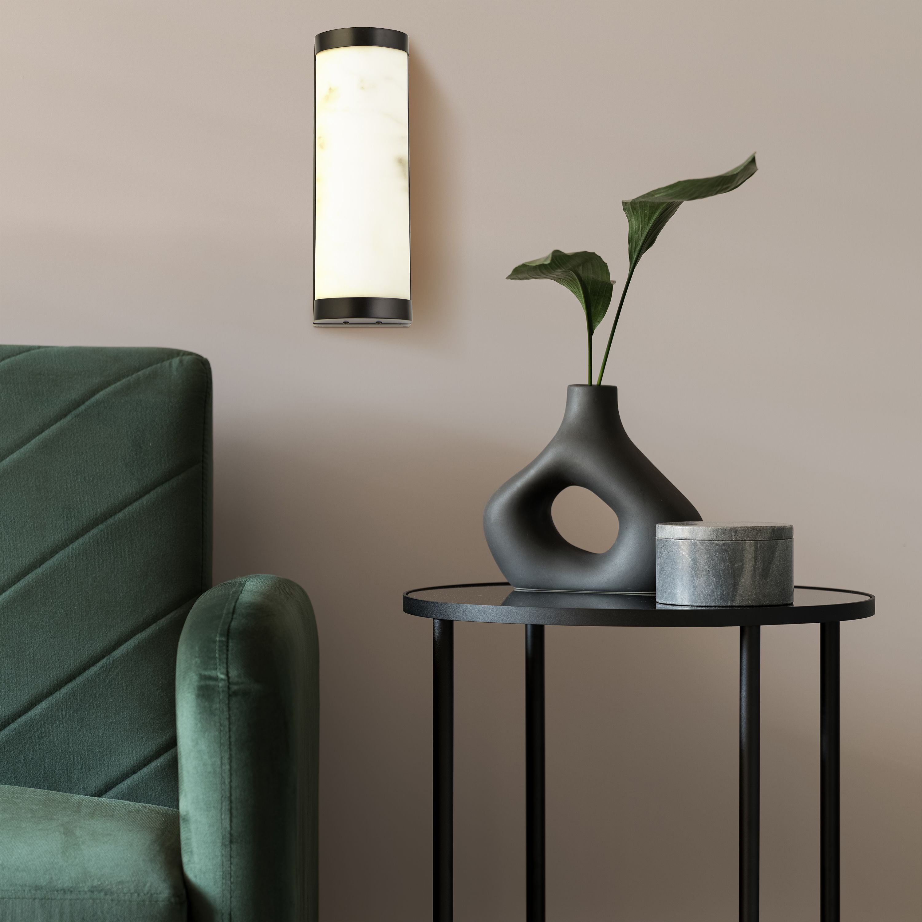 Searchlight Nile LED Wall Light 25cm in matt black styled on a beige wall beside a green velvet armchair and side table