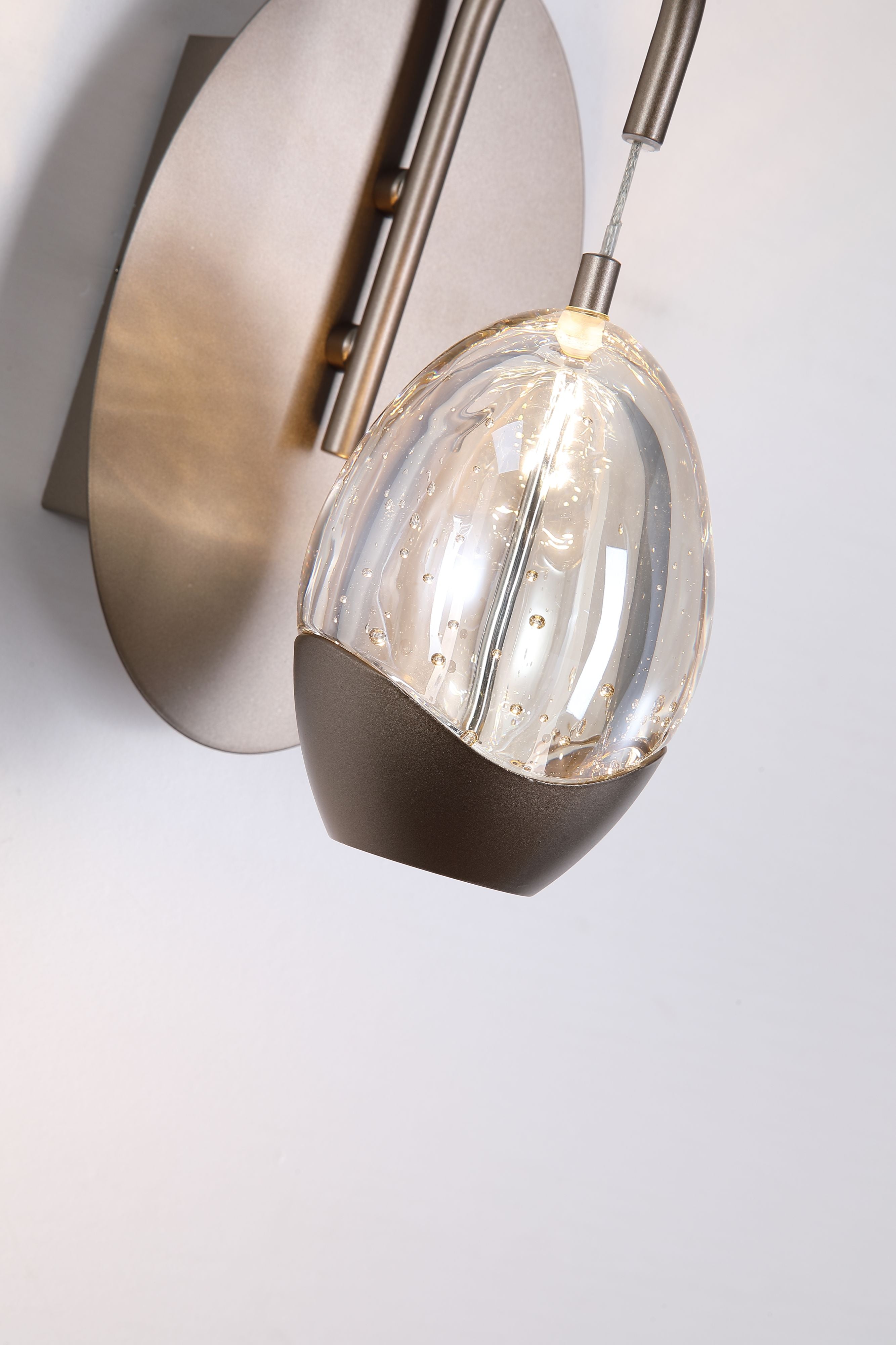 Close up of the Seeds wall light's teardrop shade, showing the bubble textured clear glass and dark bronze metal cap