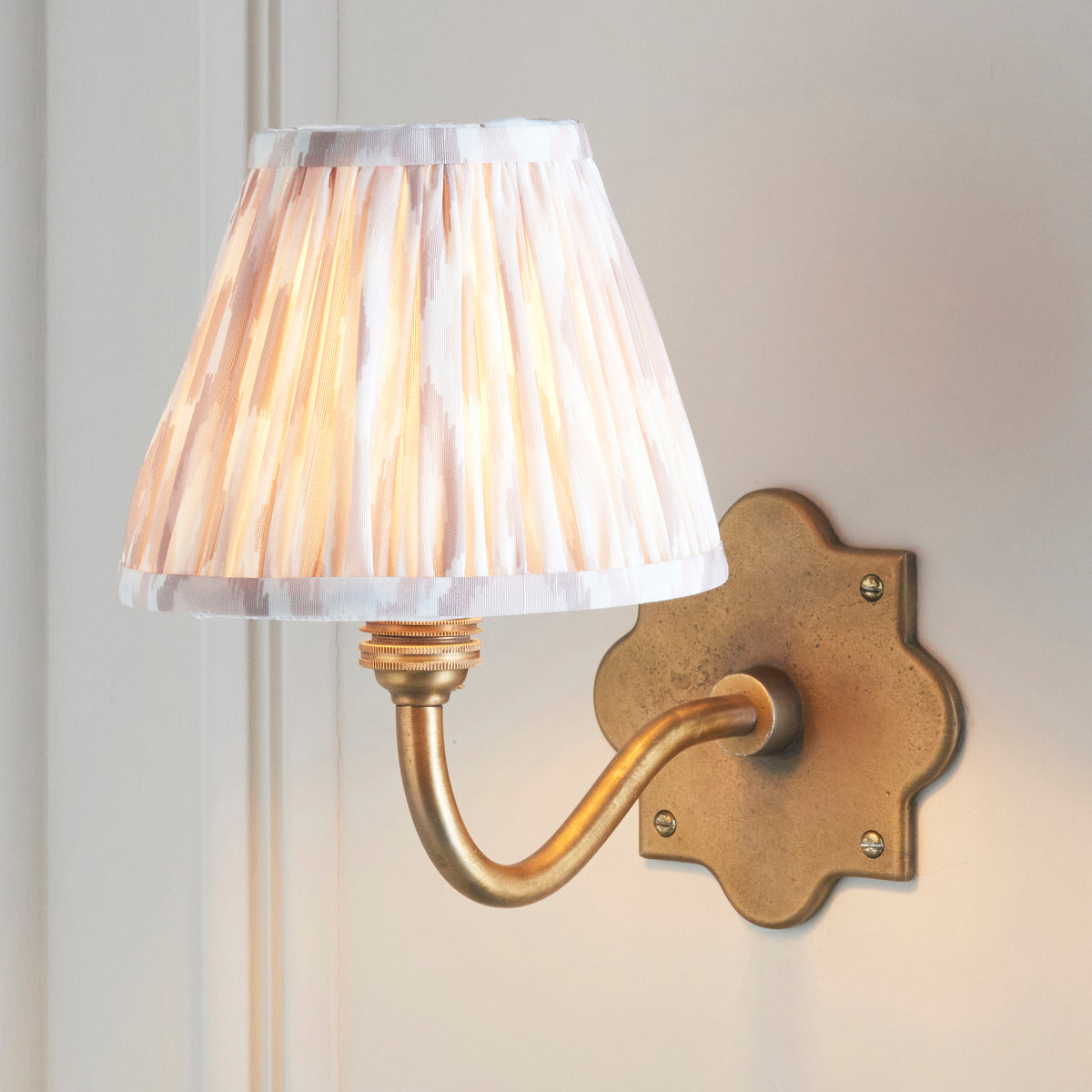 Lit Endon Anvil Curve antique brass wall light with a neutral ikat shade styled on a cream panelled wall
