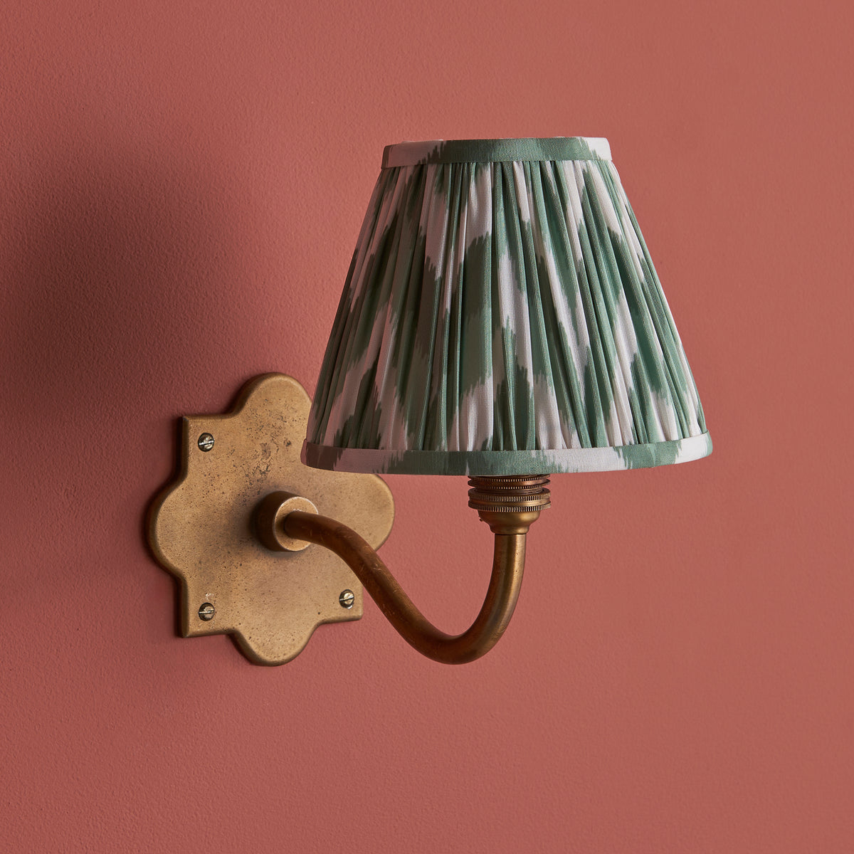 Endon Anvil Curve wall light unlit on a terracotta pink wall, antique brass scalloped backplate with Cotswold green and white zigzag shade