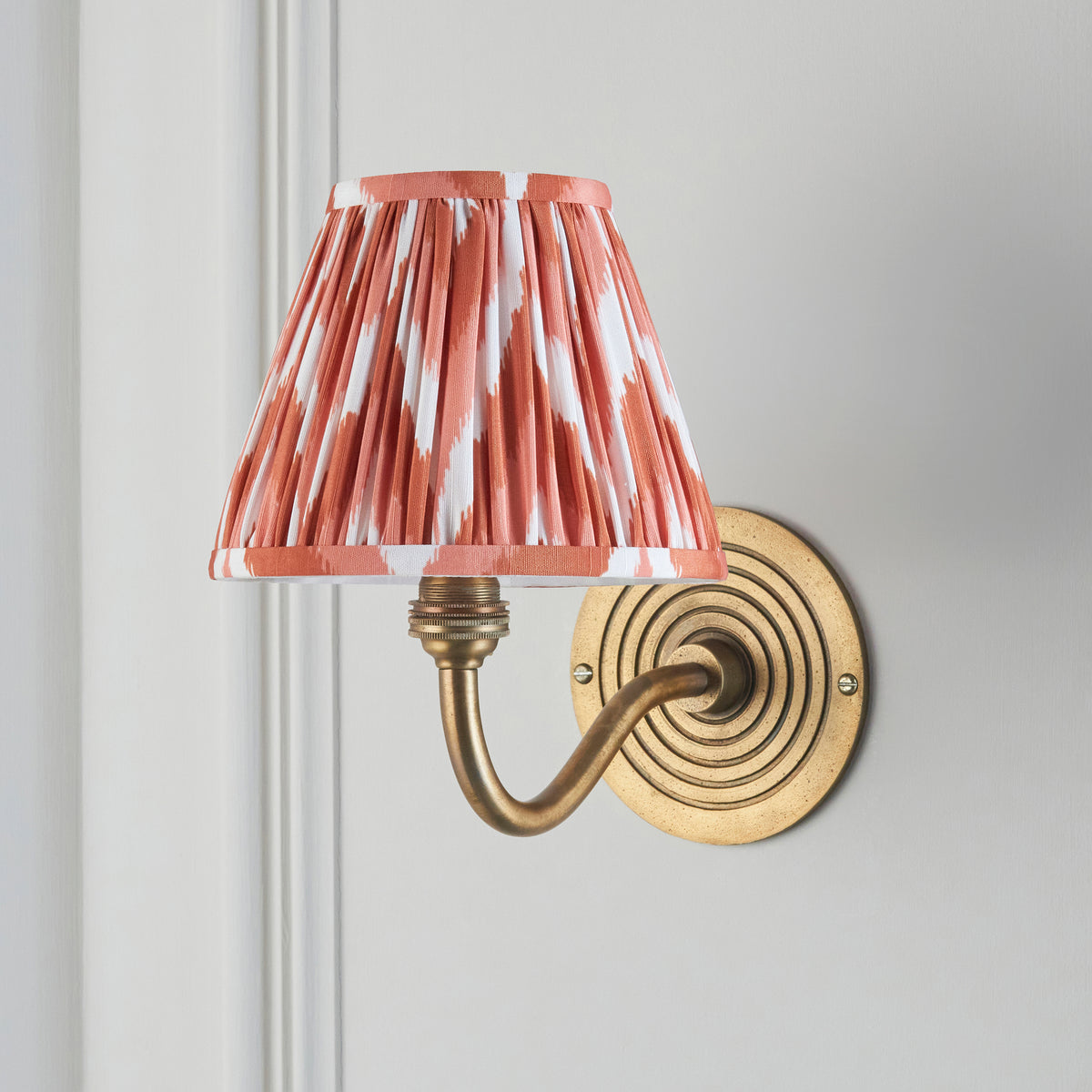 Endon Ripple Curve wall light unlit on a pale grey panelled wall, antique brass ringed backplate, swept arm and apricot orange zigzag shade