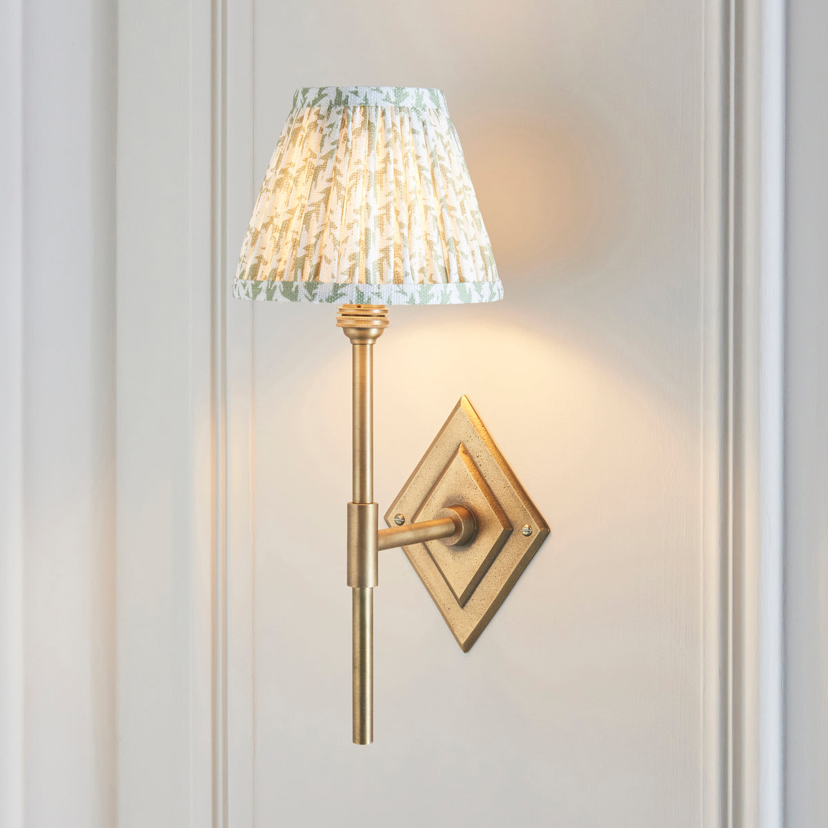 Endon Diamond Tall antique brass wall light with green leaf pleated shade lit against pale grey painted panelling