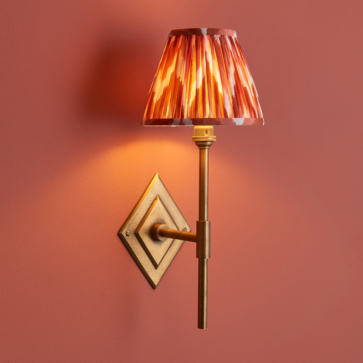 Endon Diamond Tall wall light lit against a terracotta pink wall, antique brass stem and diamond backplate with apricot orange zigzag shade