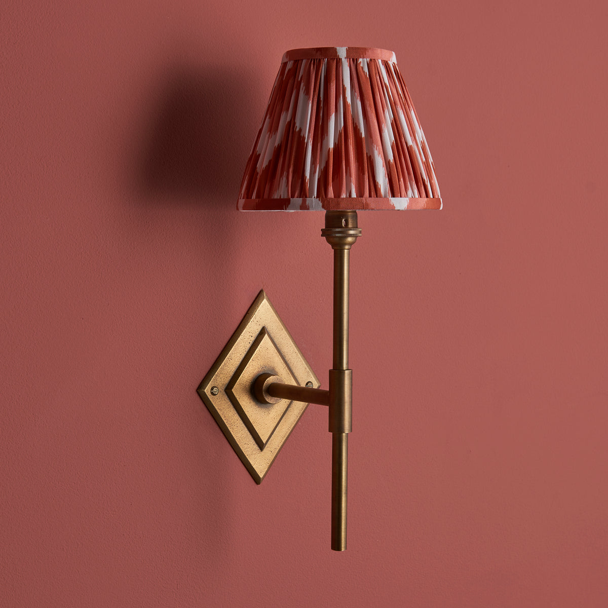 Endon Diamond Tall wall light switched off against a terracotta pink wall, antique brass finish with apricot orange and white zigzag shade