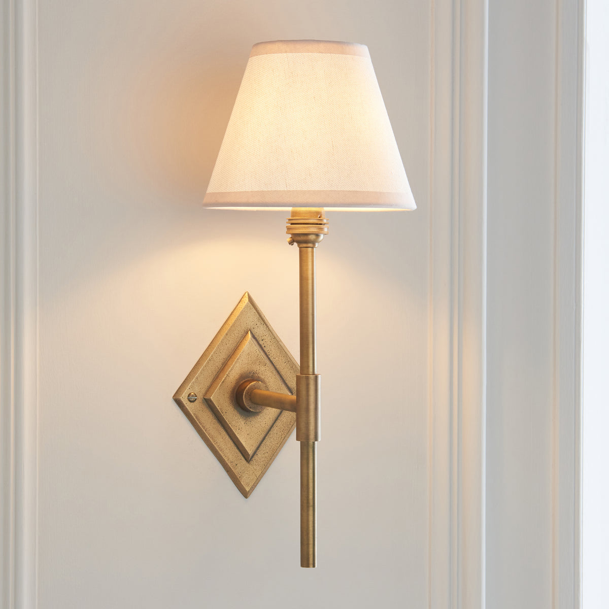 Endon Diamond Tall wall light switched on against cream panelling, warm light spilling from the vintage white shade onto the wall