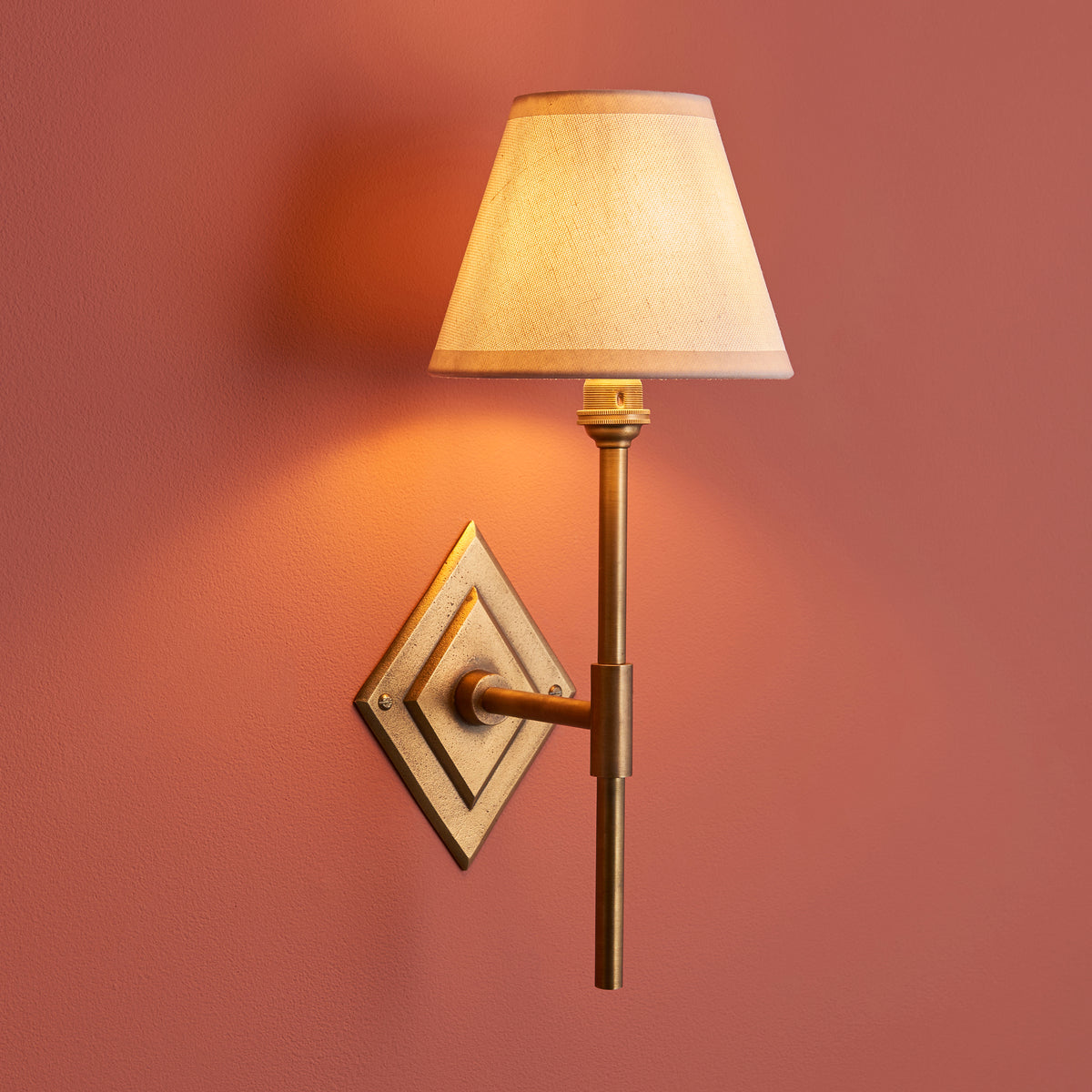 Endon Diamond Tall antique brass wall light lit on a terracotta pink wall, vintage white Ivy shade casting a warm glow