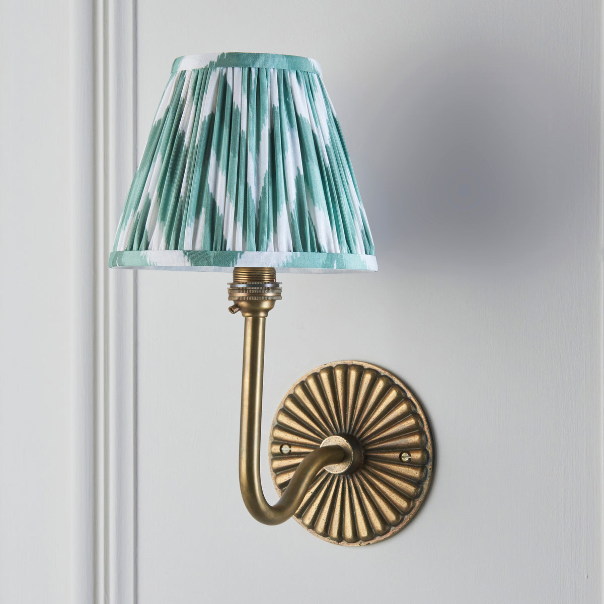 Endon Dahlia Swan wall light lit against pale grey panelling, close view of the green zigzag shade and ribbed brass backplate
