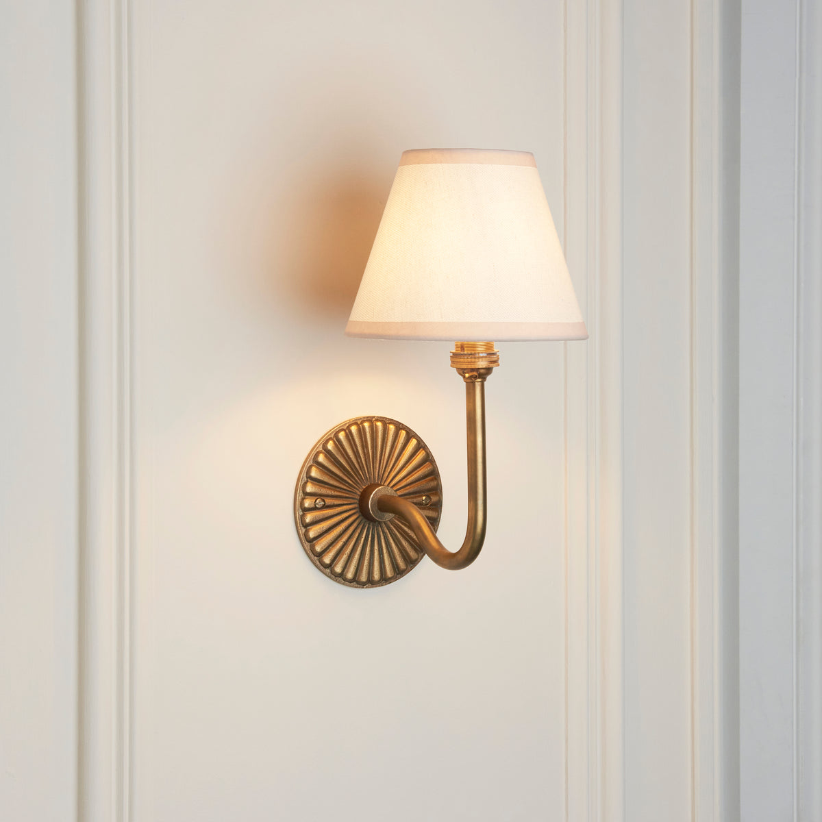 Endon Dahlia Swan antique brass wall light lit against cream wall panelling, swan neck arm curving out from the fluted backplate
