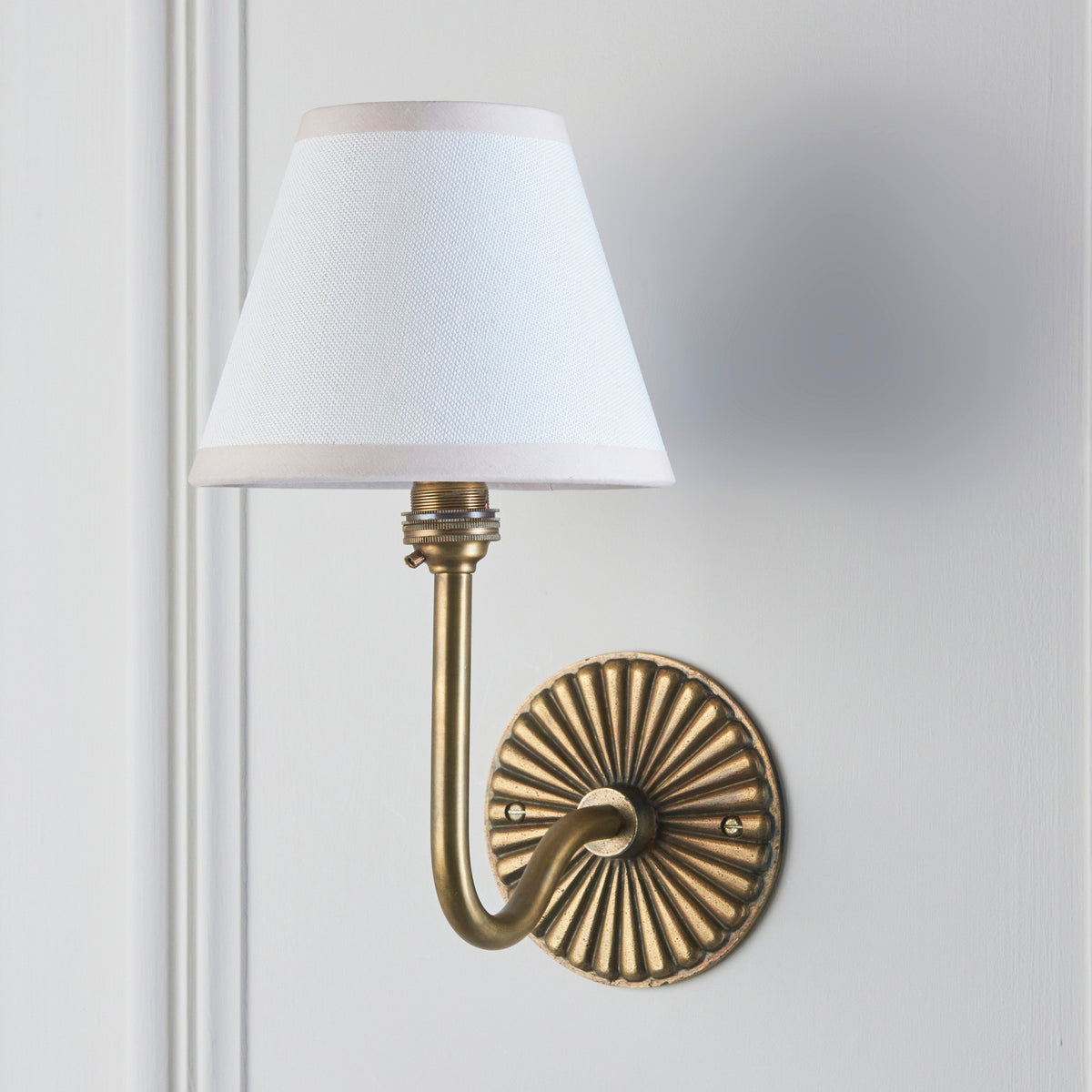Endon Dahlia Swan antique brass wall light unlit on a pale grey painted panel wall with vintage white shade
