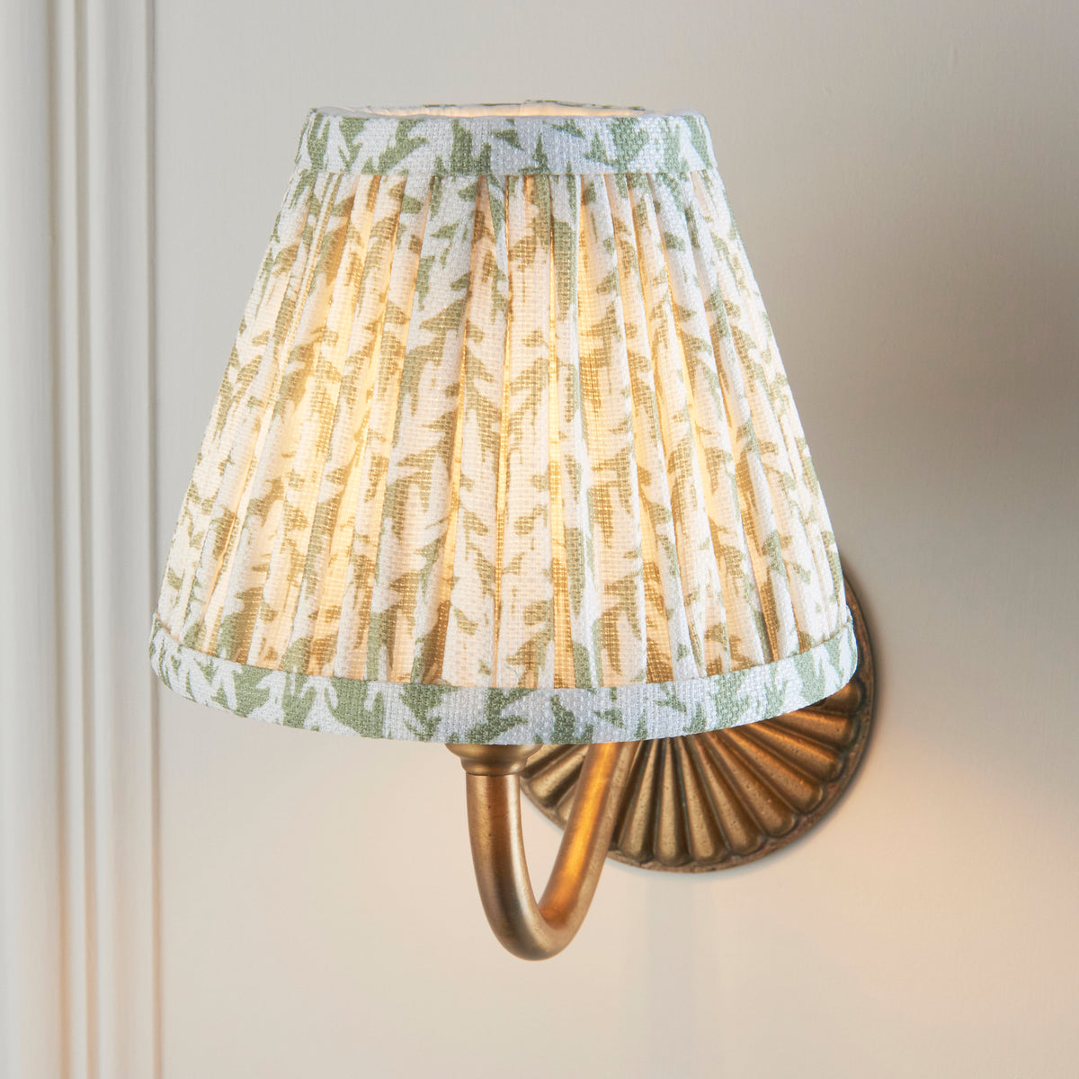 Close up of the Endon Dahlia Curve wall light lit, green leaf print pleated shade filling the frame with the brass backplate behind