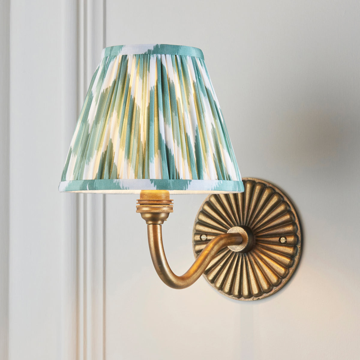 Endon Dahlia Curve antique brass wall light switched on, green zigzag shade glowing against a pale grey panelled wall