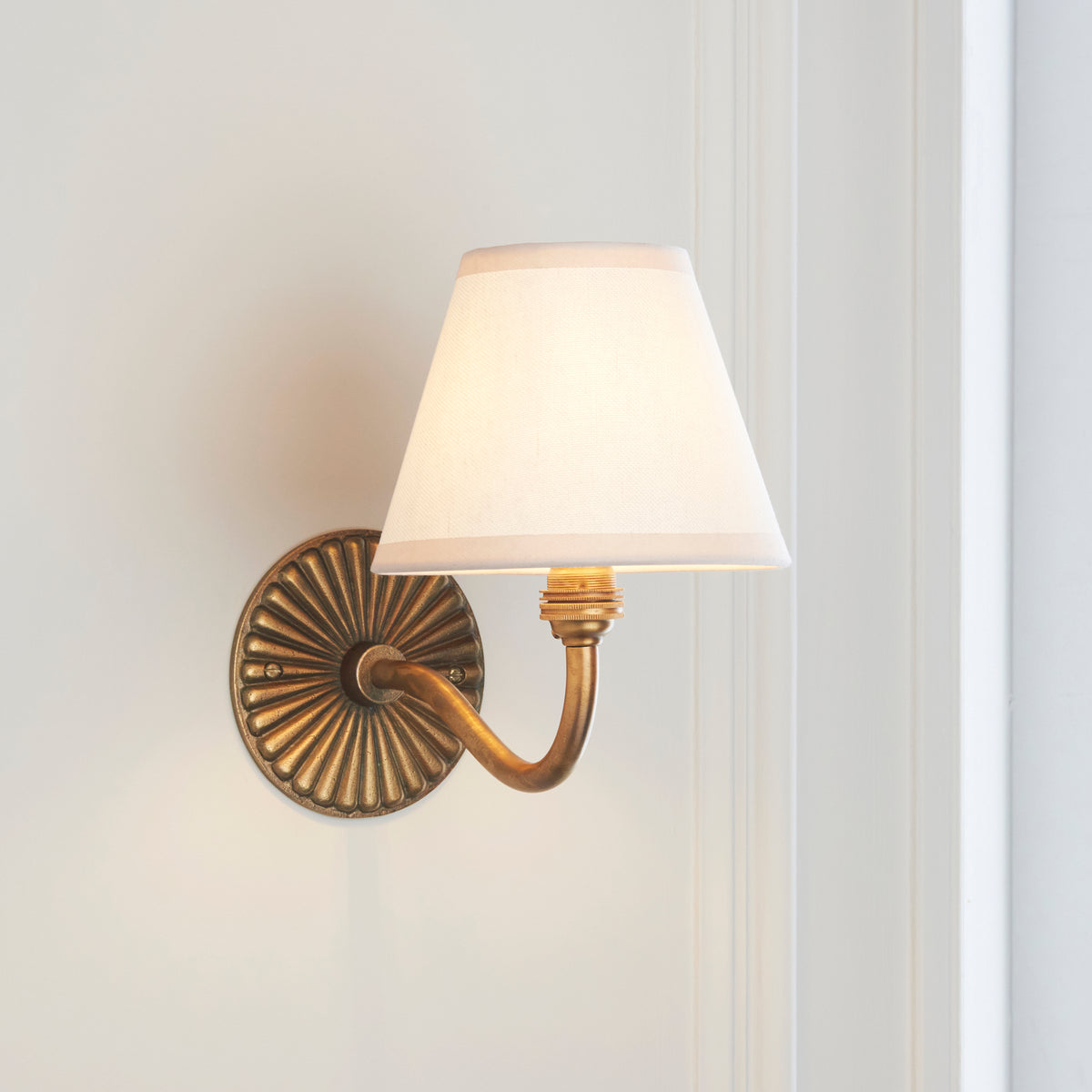 Endon Dahlia Curve antique brass wall light unlit on a cream panelled wall, showing the curved arm and vintage white Ivy shade