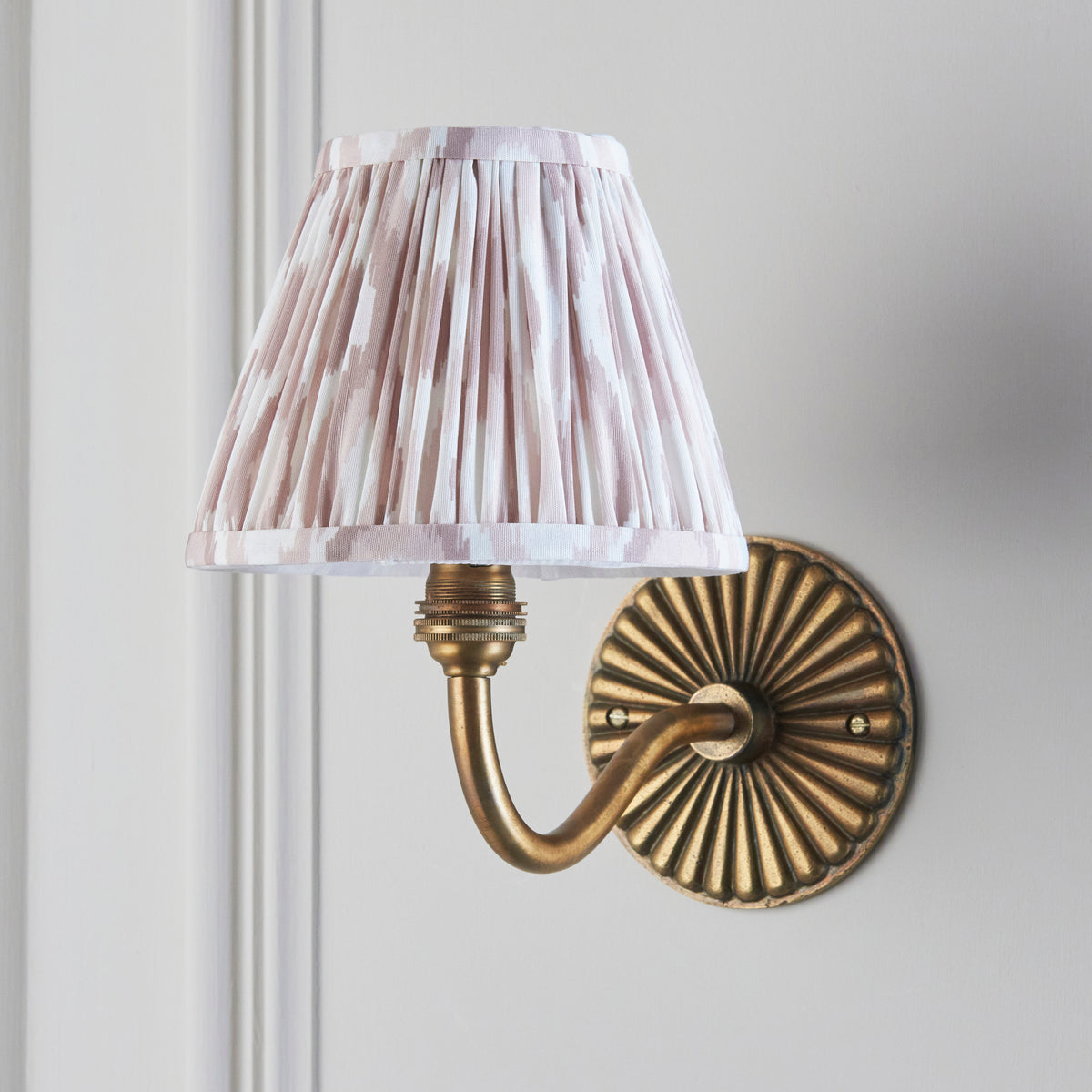 Endon Dahlia Curve wall light unlit on a cream panelled wall, pink and off white ikat shade over antique brass arm