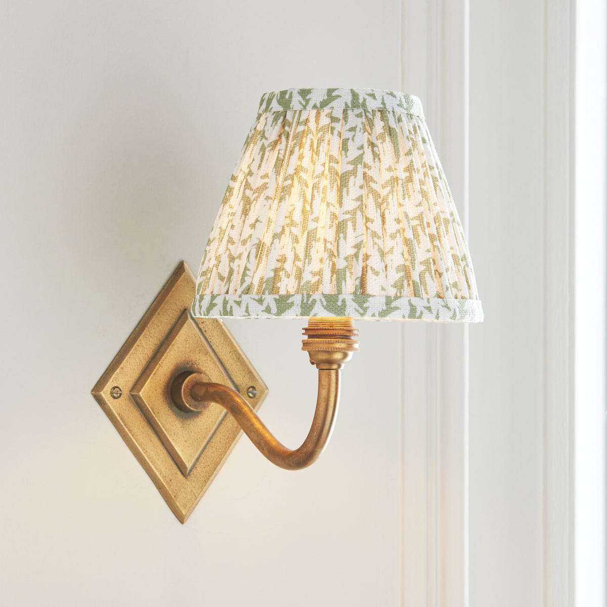 Endon Diamond Curve wall light lit against cream wall panelling, antique brass diamond backplate and herb garden green pleated shade