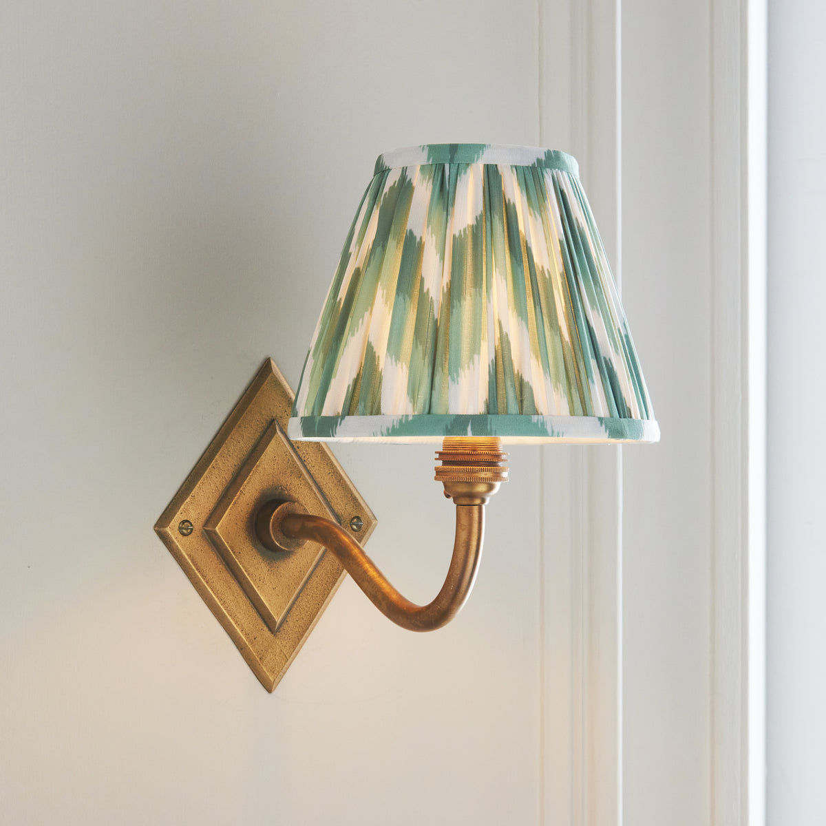 Endon Diamond Curve wall light lit on a panelled wall, curved antique brass arm sweeping to the right under the Cotswold green zigzag shade