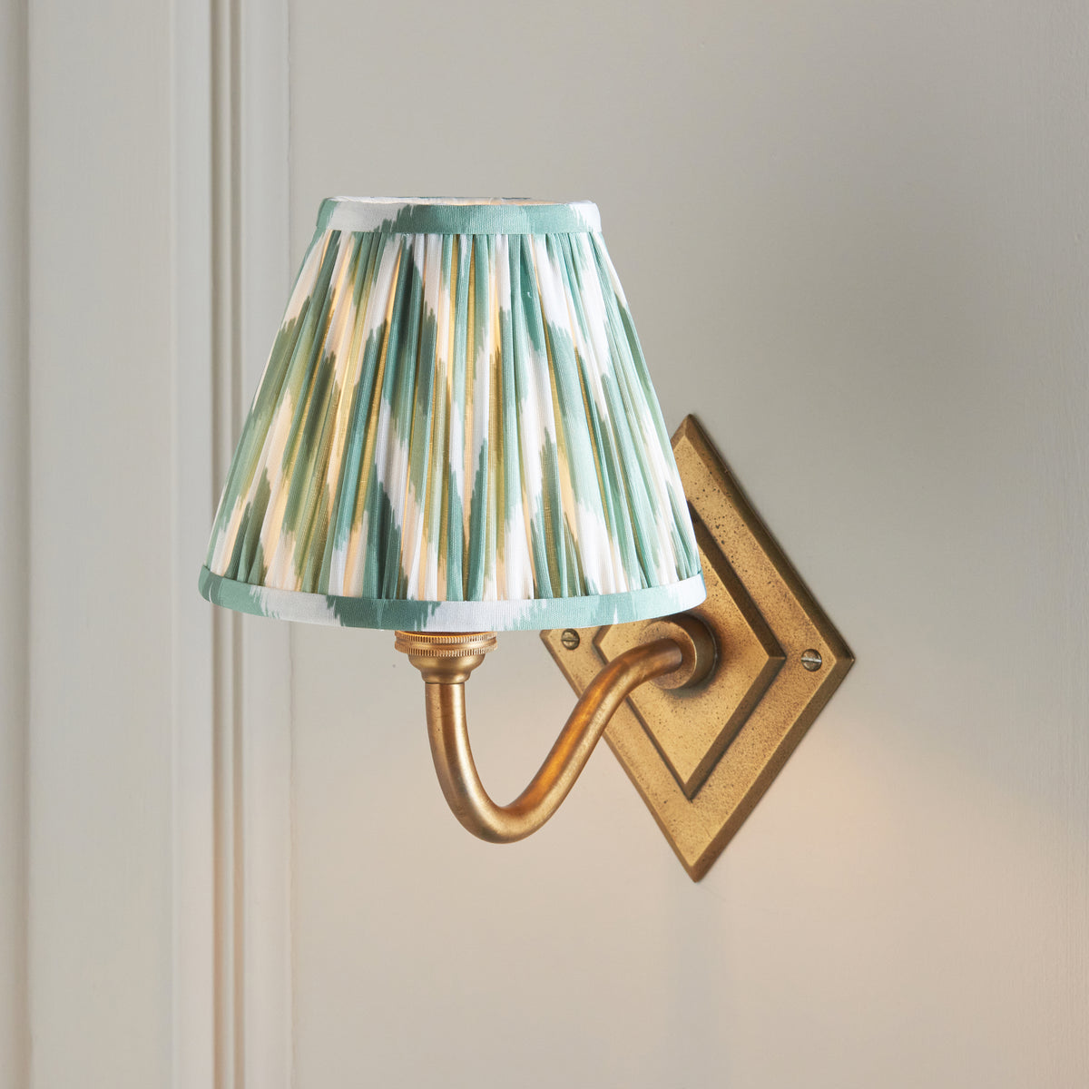 Close view of the Endon Diamond Curve wall light lit, showing the pleats of the green zigzag shade and the brass patina backplate