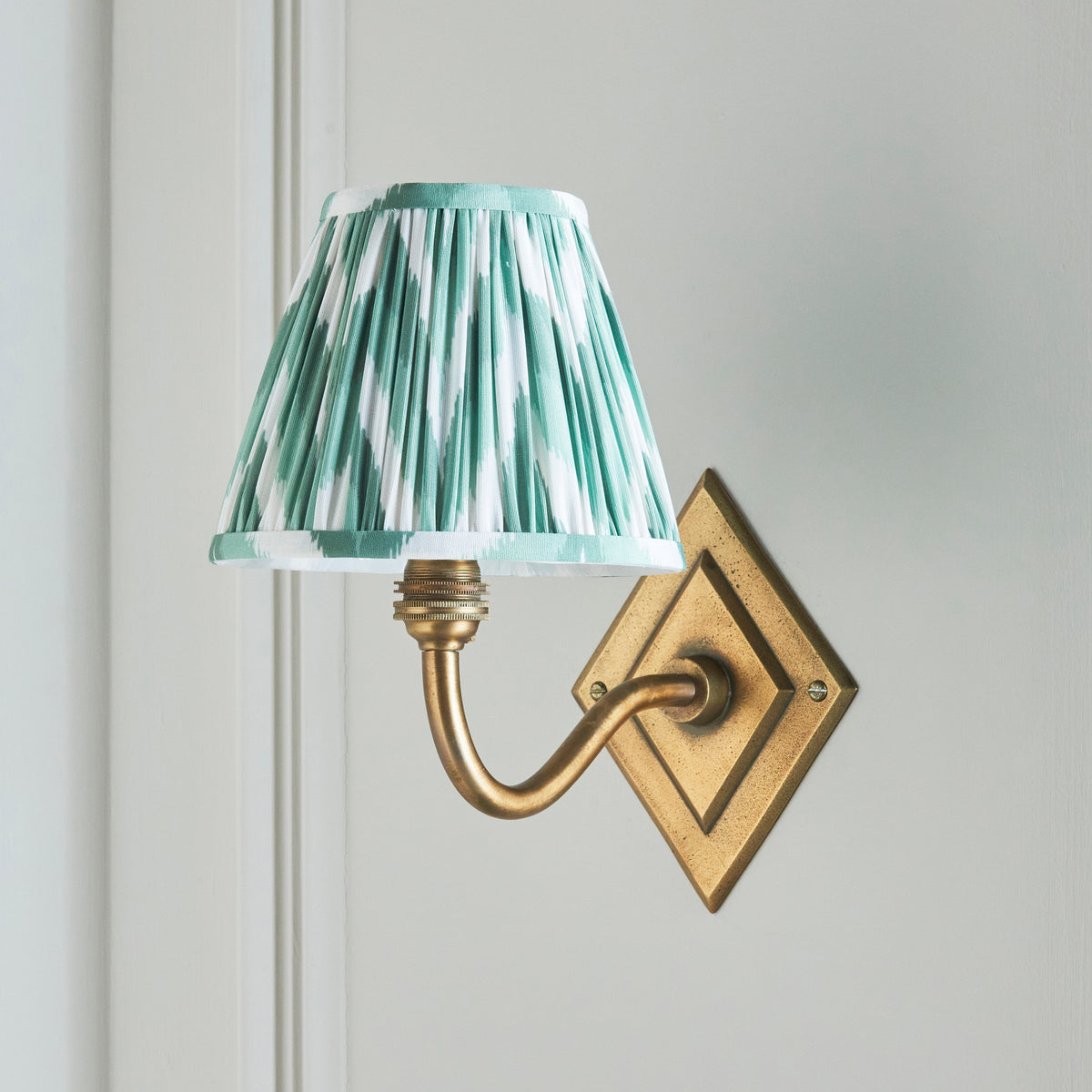 Endon Diamond Curve wall light switched off on a pale panelled wall, showing the crisp green and white zigzag print and antique brass arm