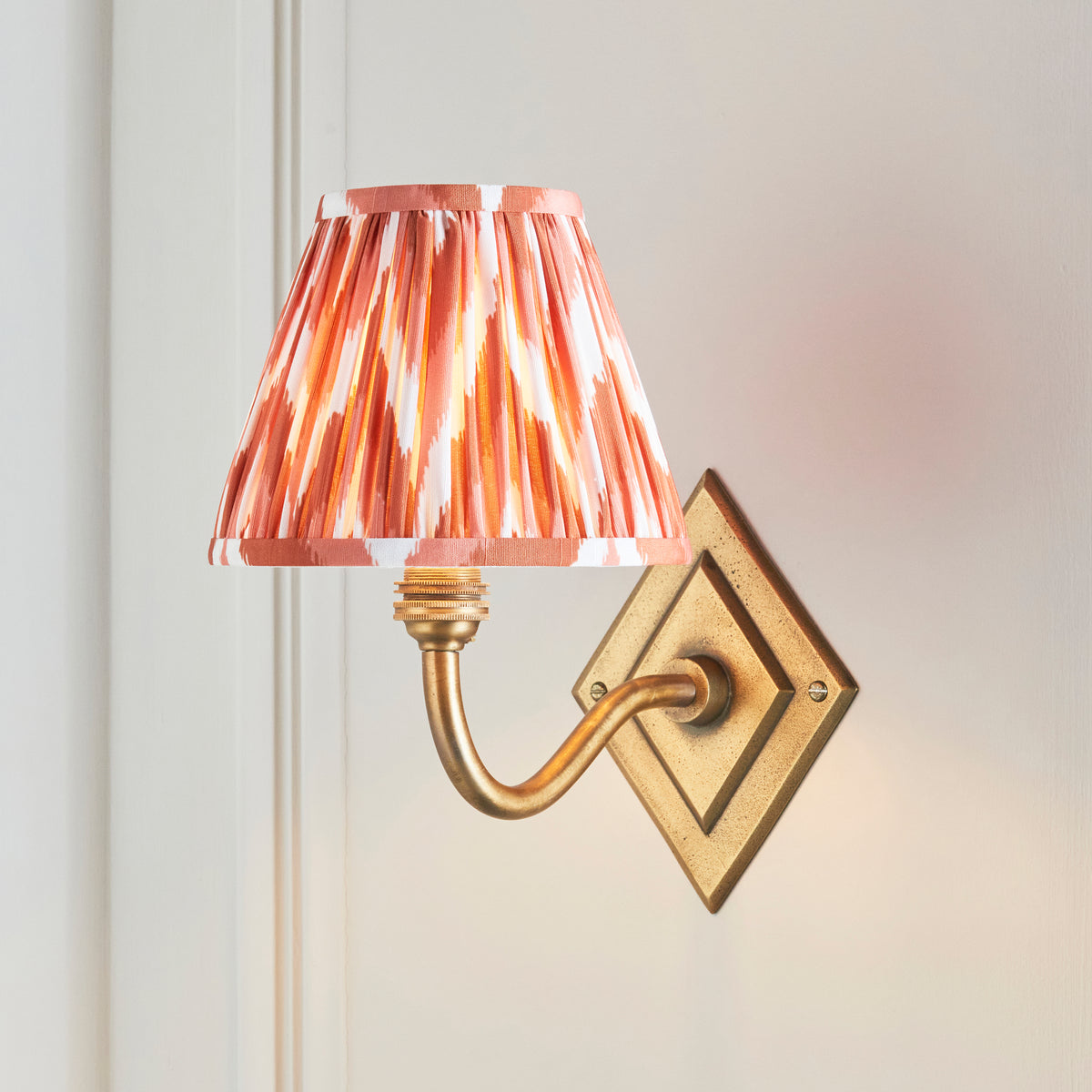 Endon Diamond Curve antique brass wall light switched on, apricot orange zigzag shade glowing against a cream panelled wall