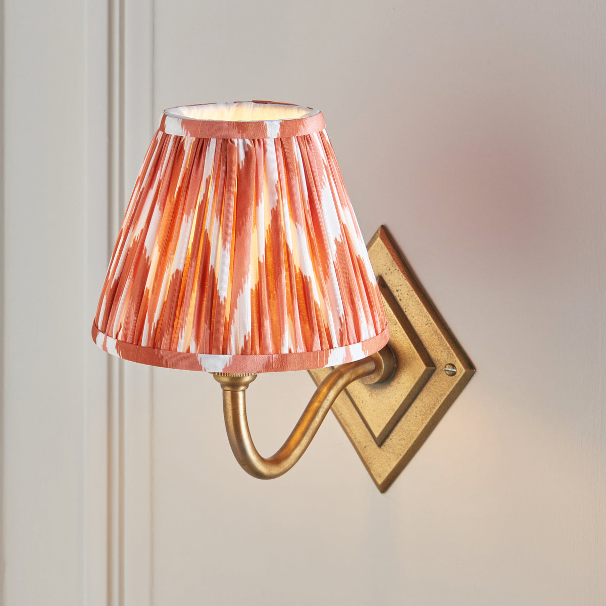 Close up of the Endon Diamond Curve wall light lit, apricot orange zigzag pleated shade with its pale inner lining visible through the top opening