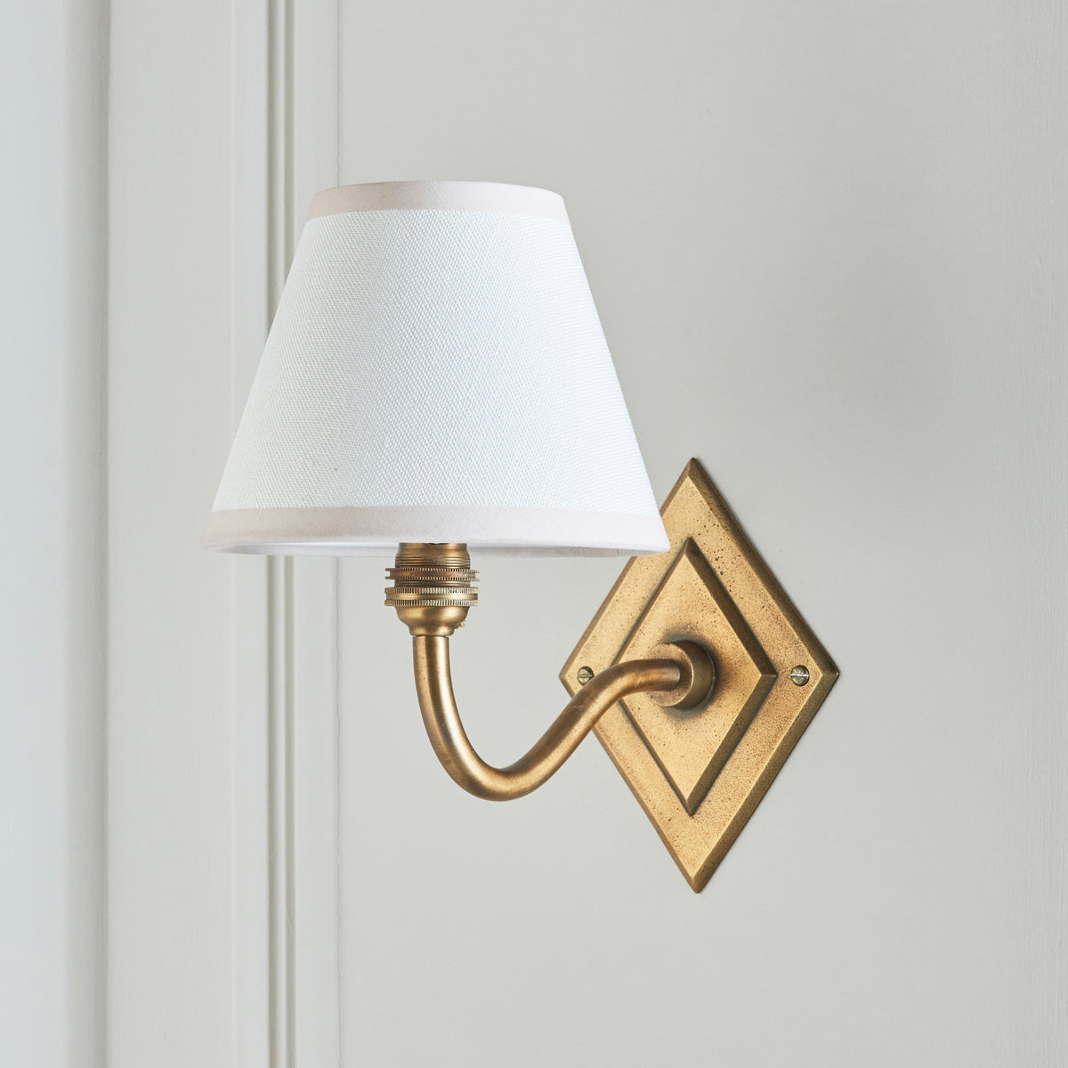 Endon Diamond Curve wall light switched off on a grey green panelled wall, showing the antique brass arm and white Ivy shade